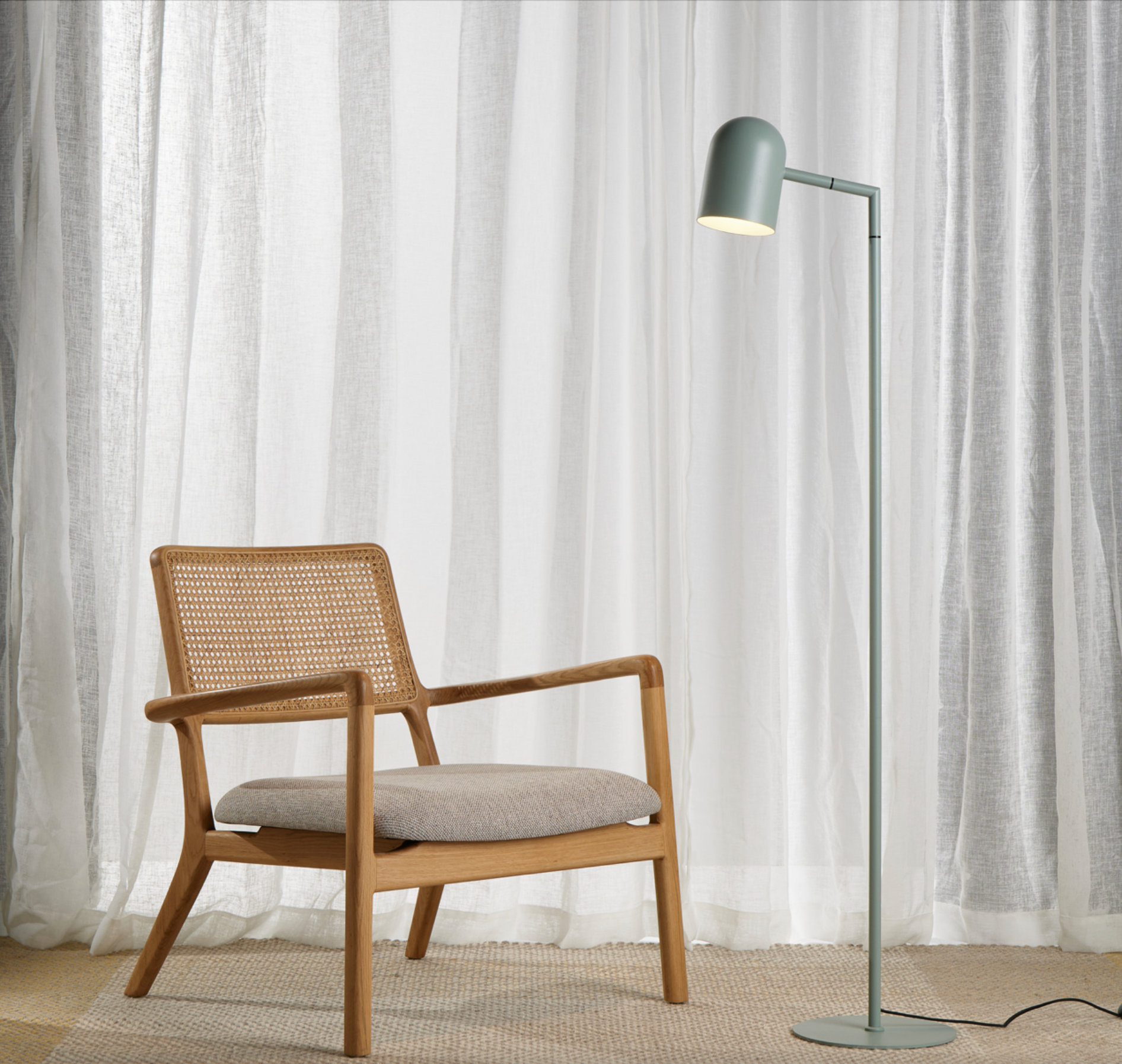 Wooden armchair with a grey cushion and a floor lamp against white curtains.