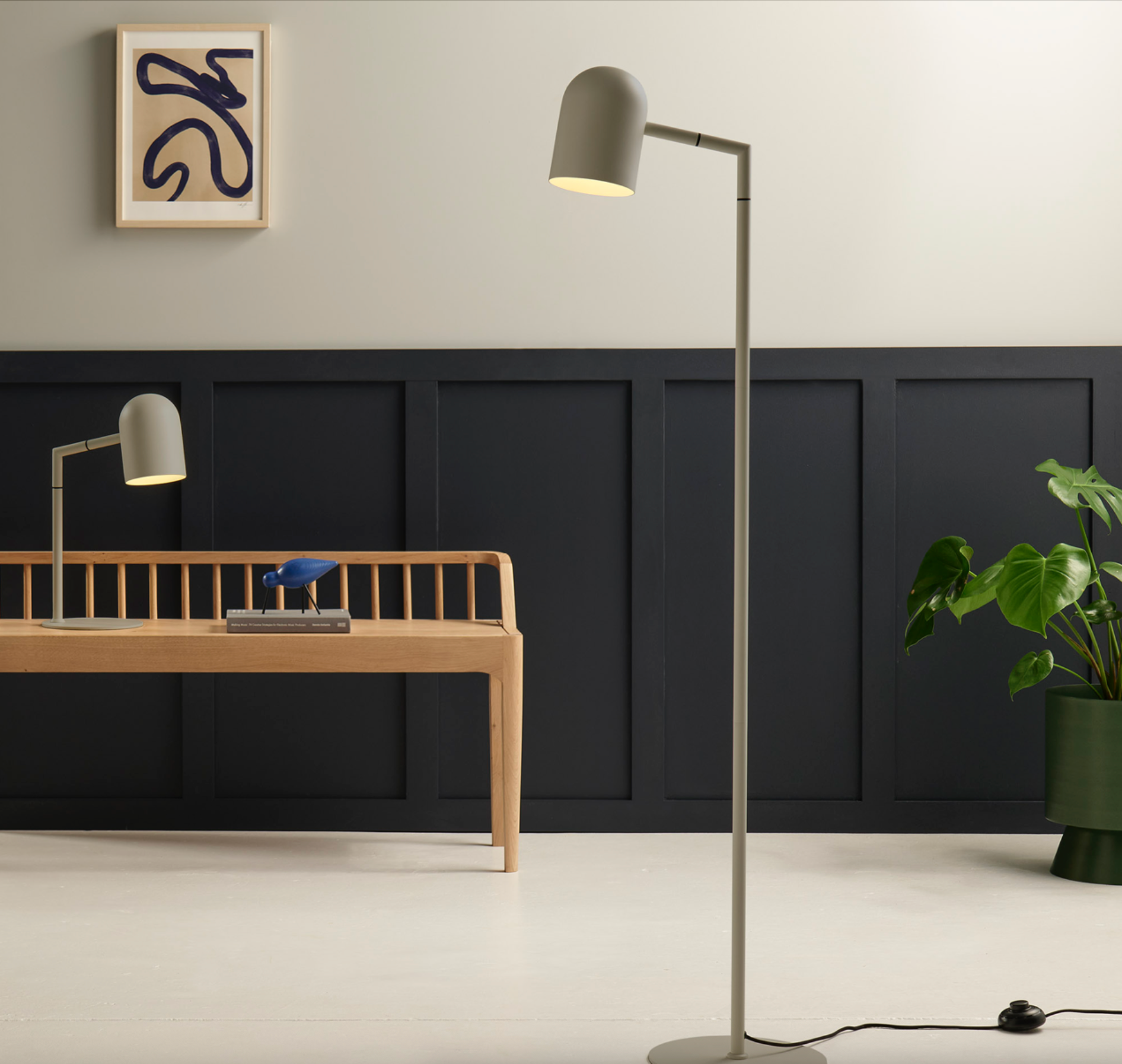 Modern interior with a floor lamp, desk, and plant against a black and white wall.