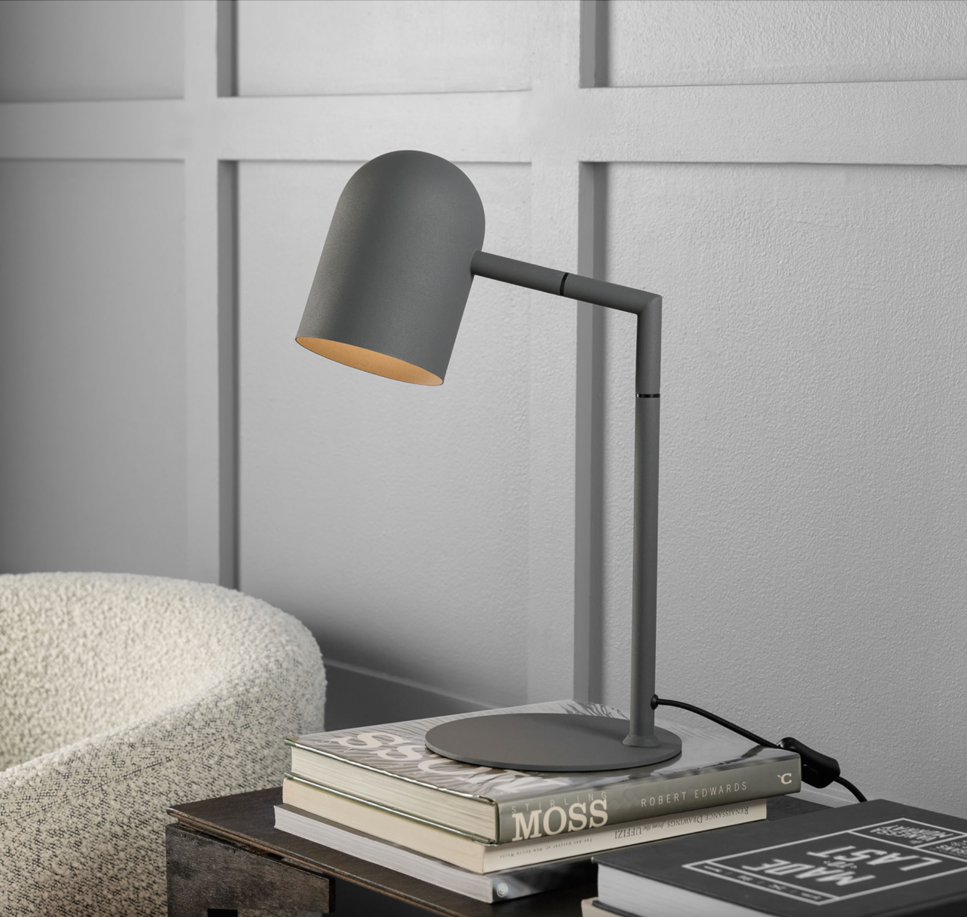 Grey desk lamp on a stack of books with a textured wall background