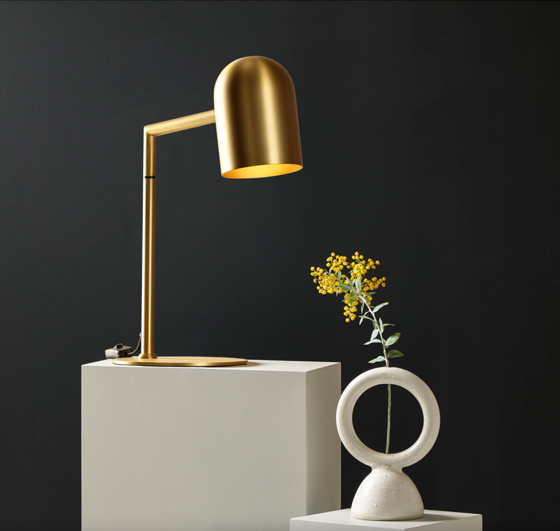 Gold desk lamp on a white pedestal with a black background
