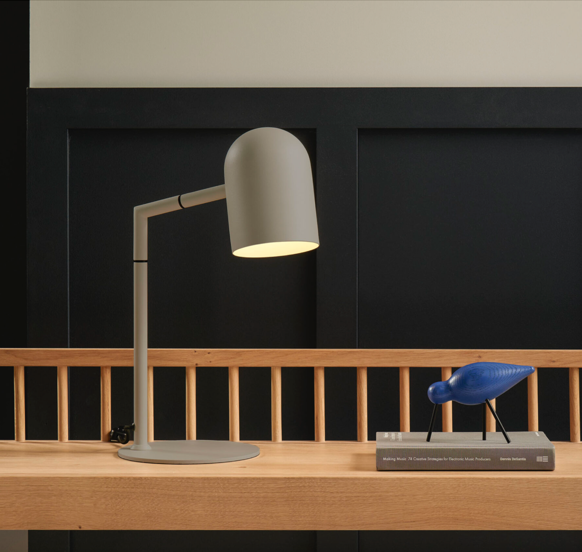 Modern grey desk lamp on a wooden surface with a black wall background