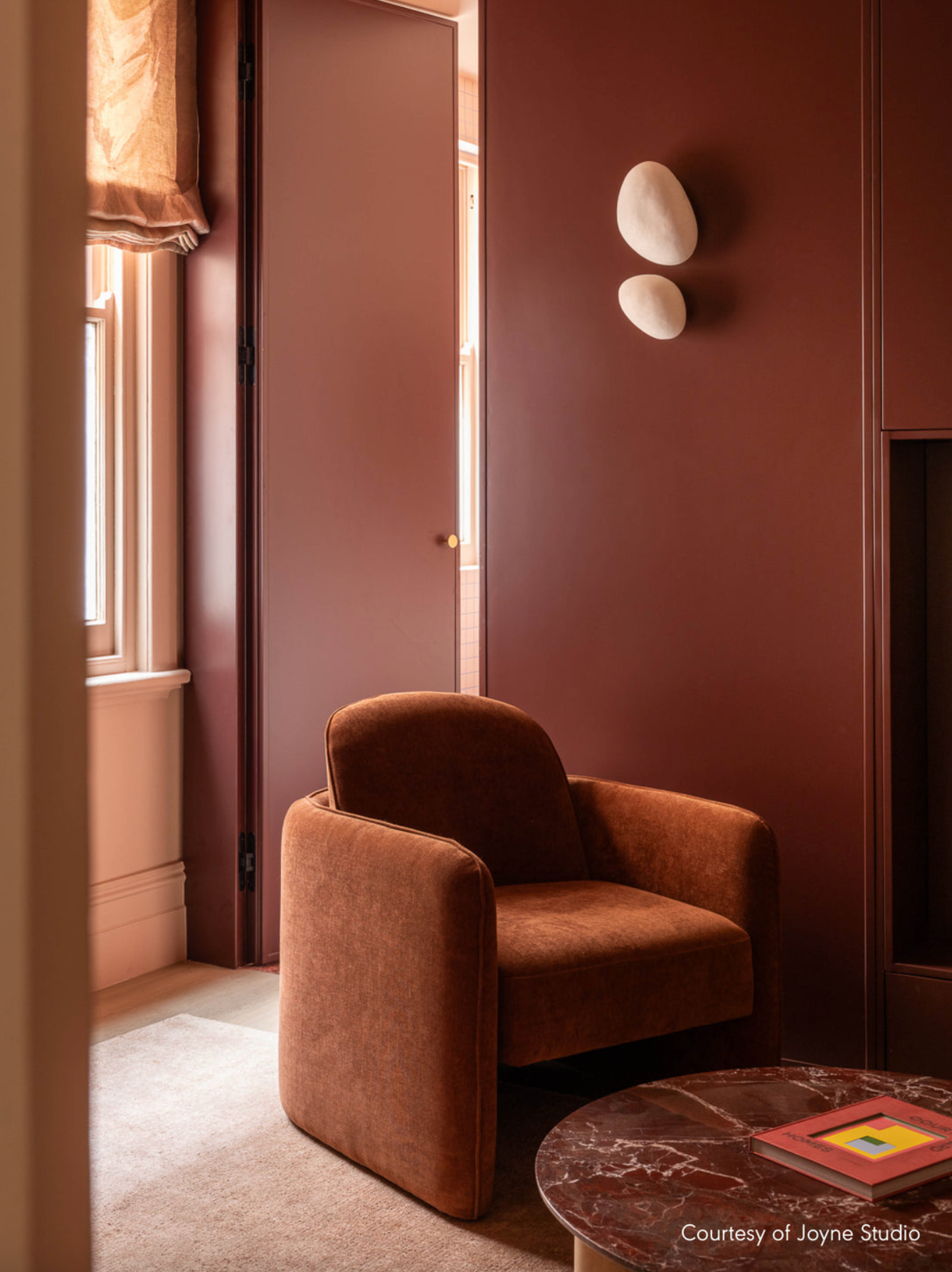 Brown armchair in a room with a textured wall and a small table and wall lights. 