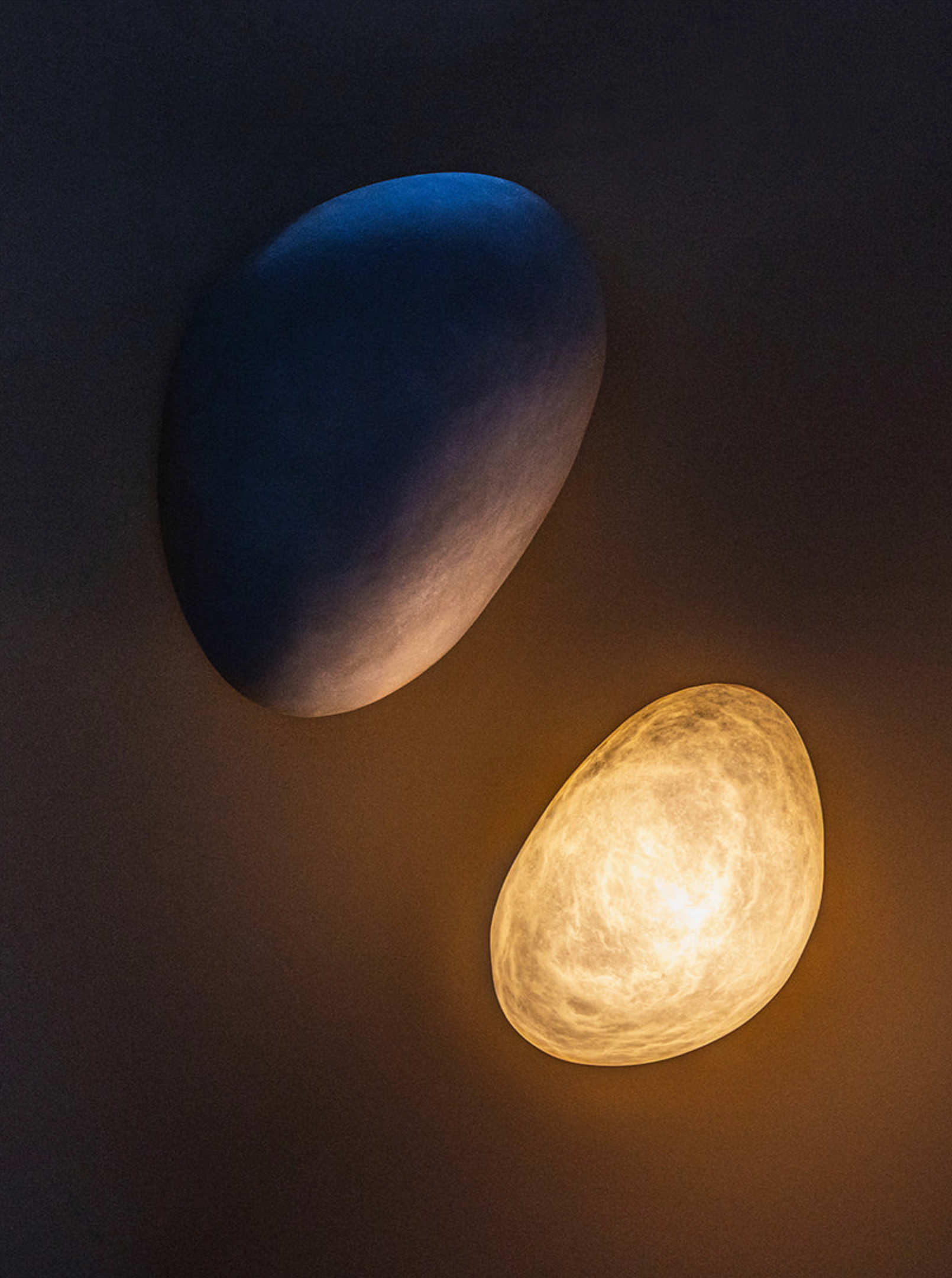 Two wall lights one glowing yellow on a dark background.
