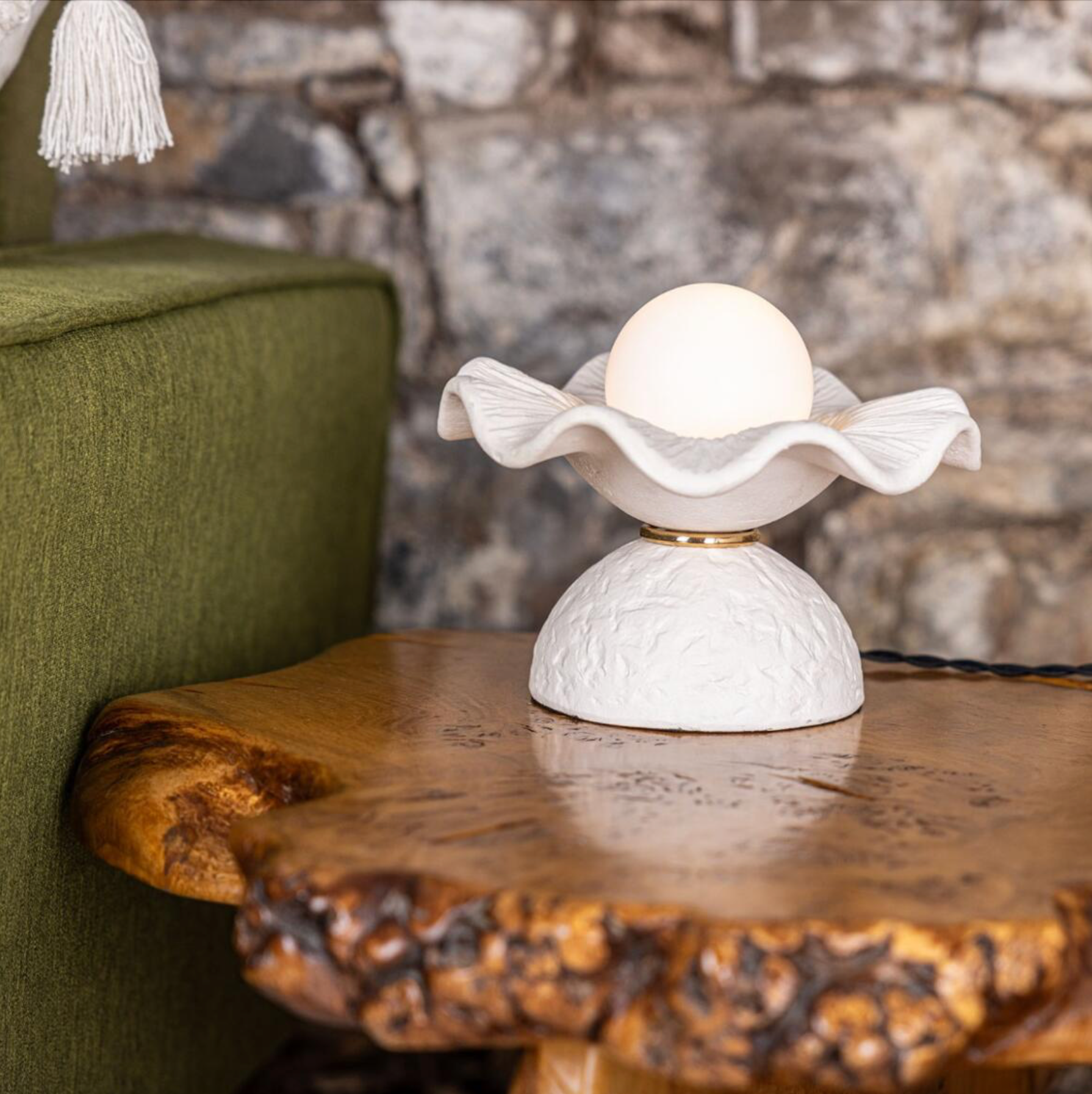 White table lamp with decorative design on a wooden surface against a stone wall.