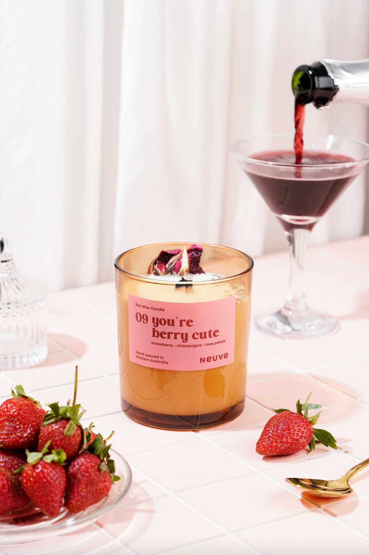 Candle labeled '09 you're berry cute' with strawberries and a glass of red wine on a table.