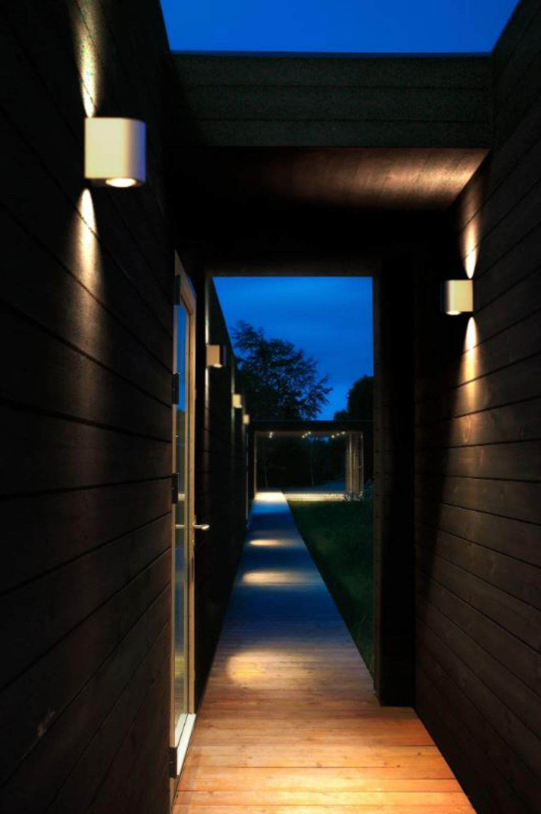 Modern outdoor hallway with wooden floor and dark walls, leading to a blue sky.