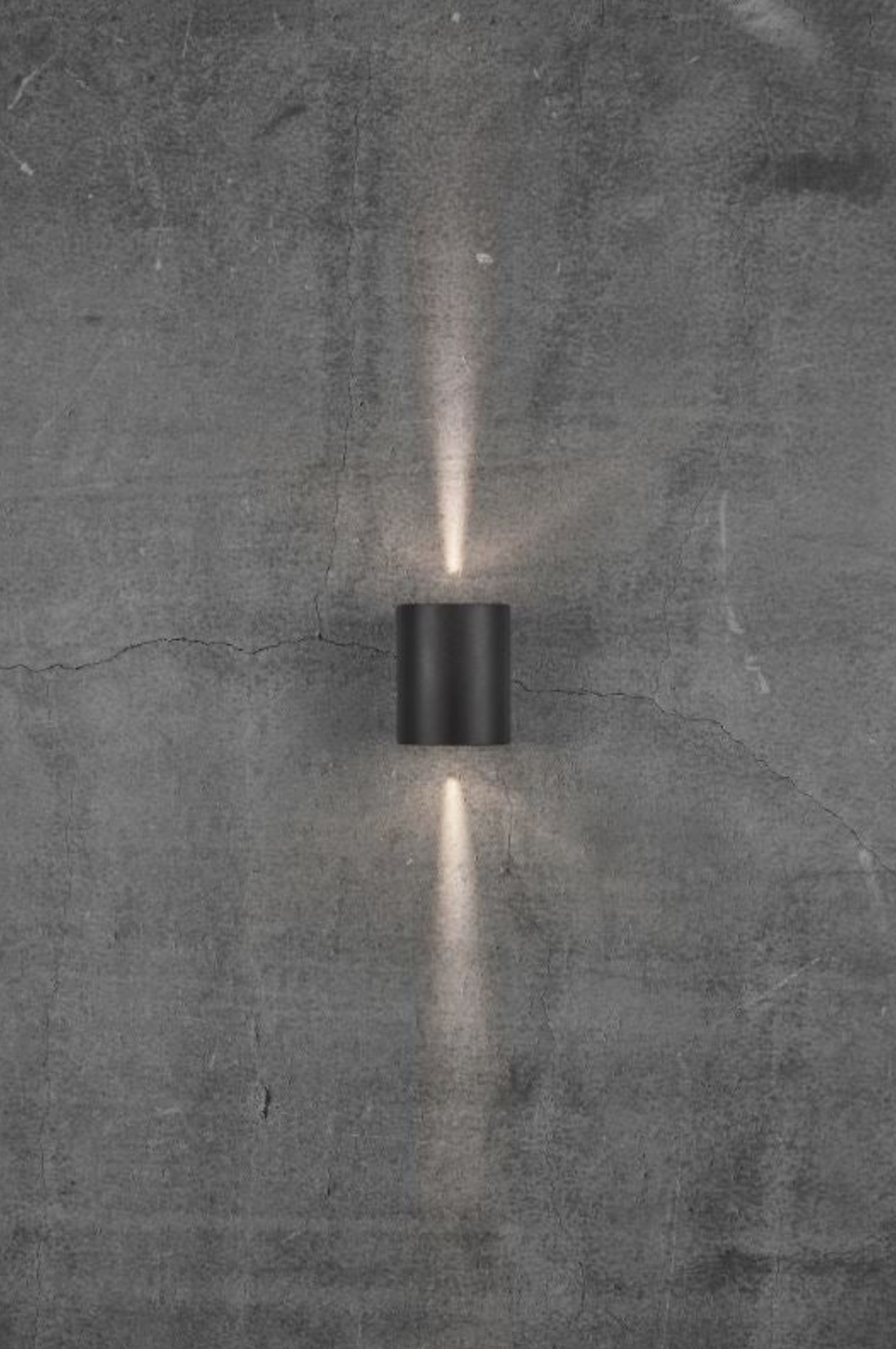 Black cylindrical wall light fixture on a textured gray wall