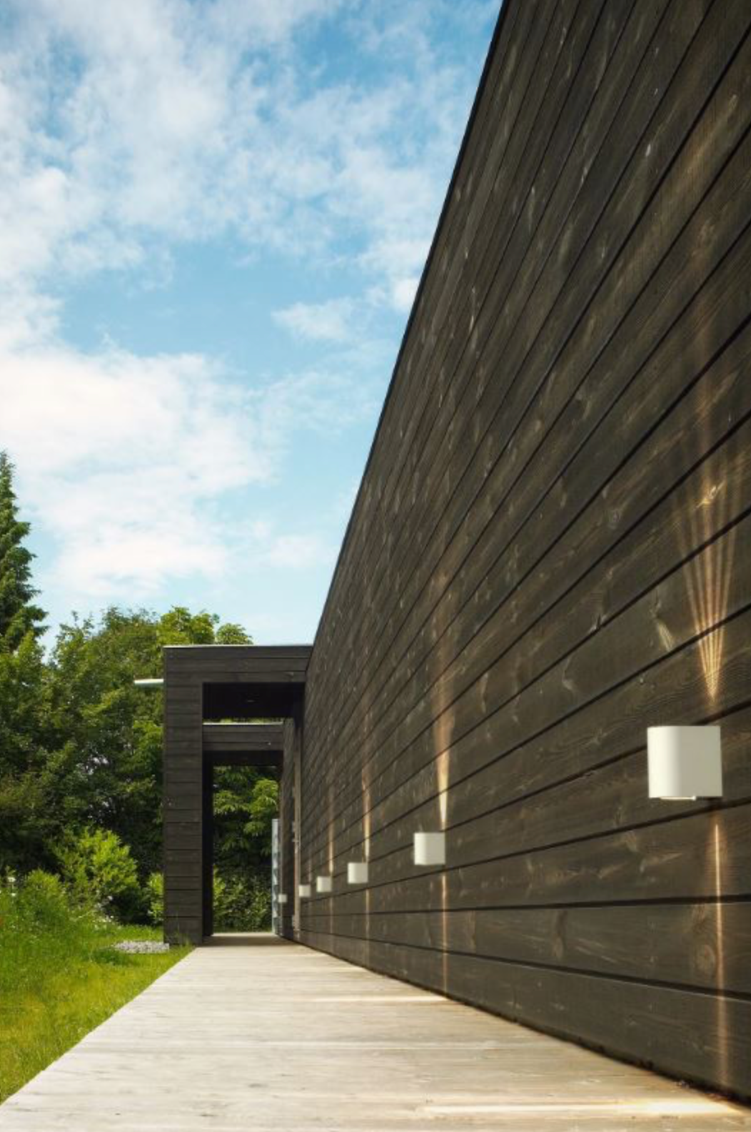 Modern building with dark wooden facade and white walkway under a blue sky.