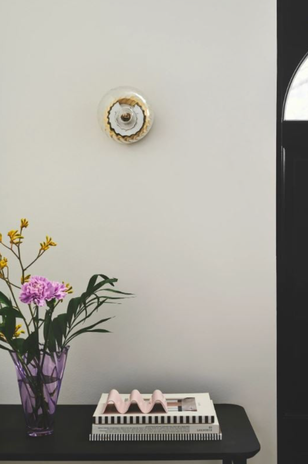 Decorative wall light with a vase of flowers and a small table with items on a light grey wall.