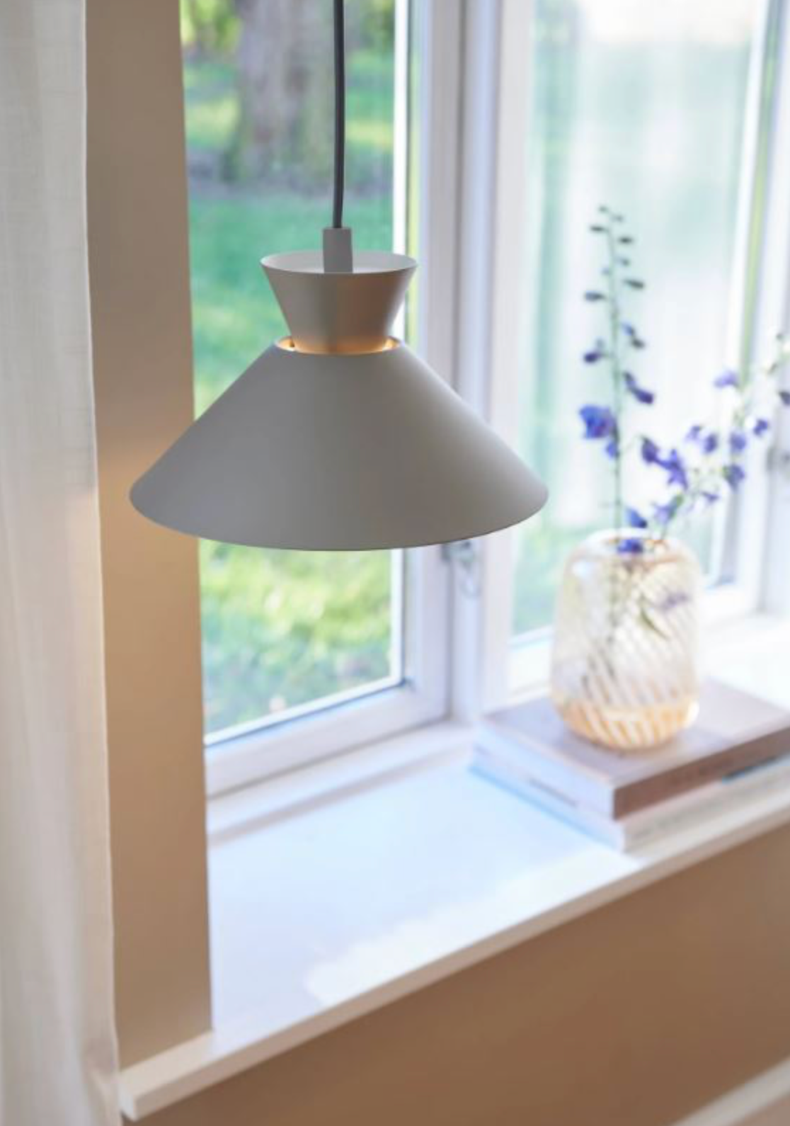 Grey pendant lamp hanging by a window with a vase of flowers on the windowsill.