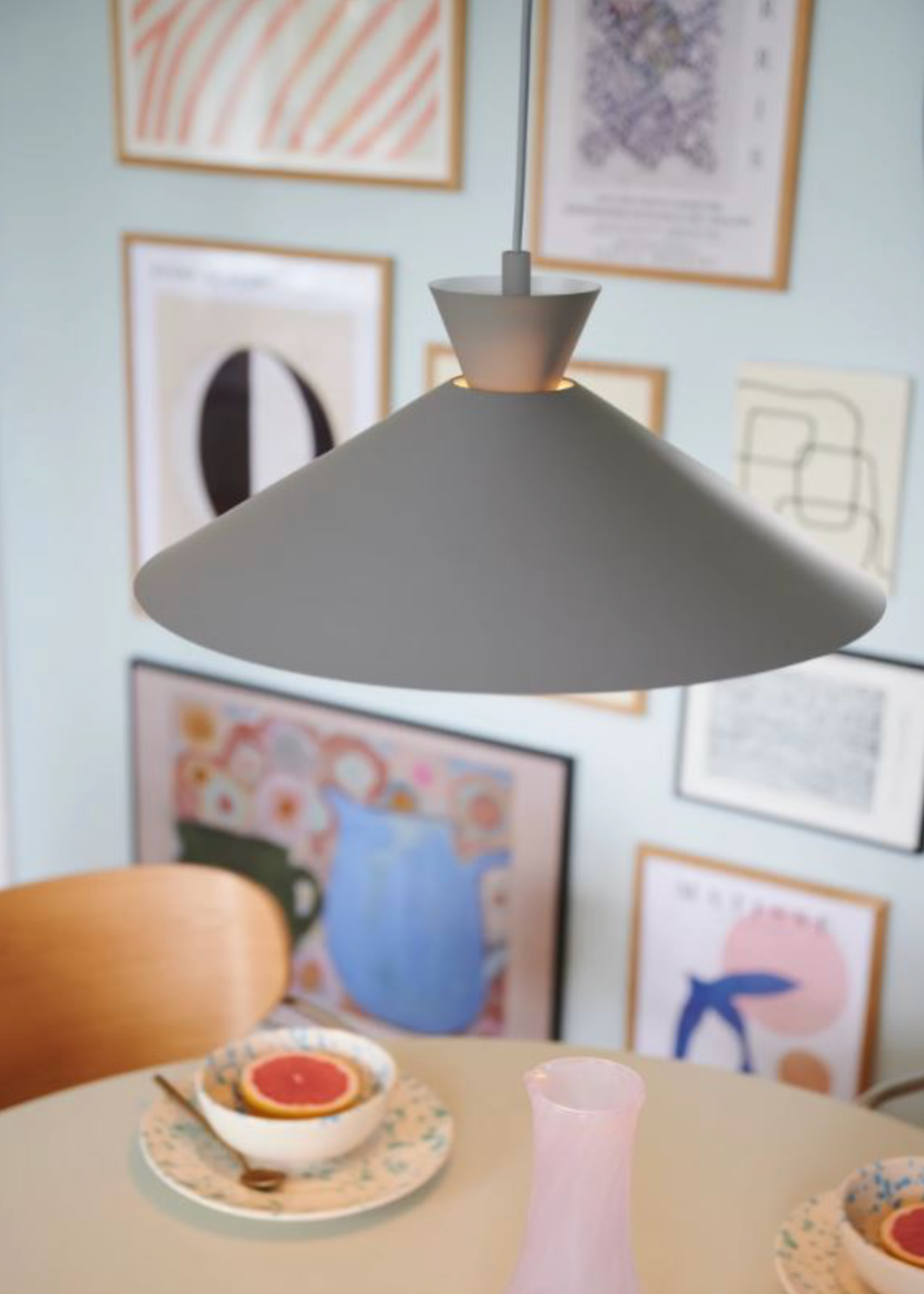 Grey pendant light over a dining table with a teacup and saucer, surrounded by framed abstract art on the wall.