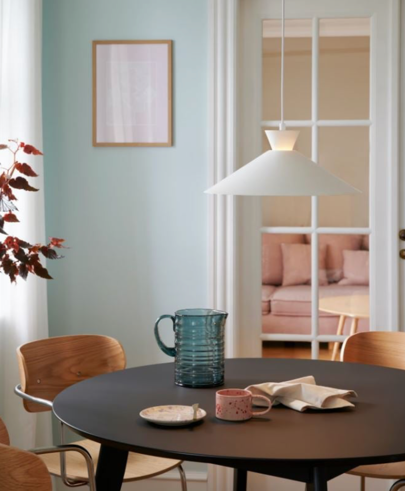 Dining area with a round table, chairs, and a vase in a room with light blue walls.