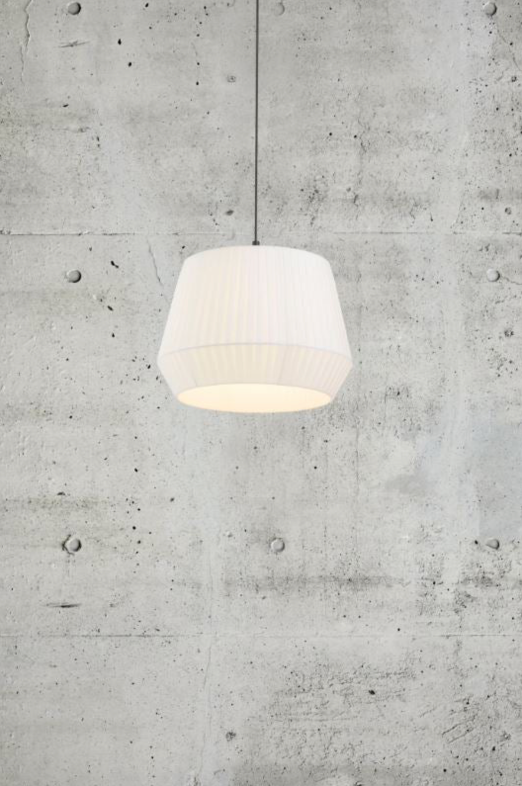 White pleated fabric pendant light hanging against a concrete wall