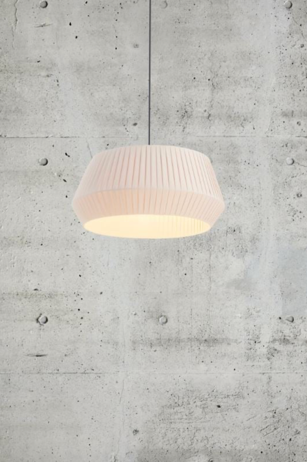 White pleated fabric pendant light against a concrete wall