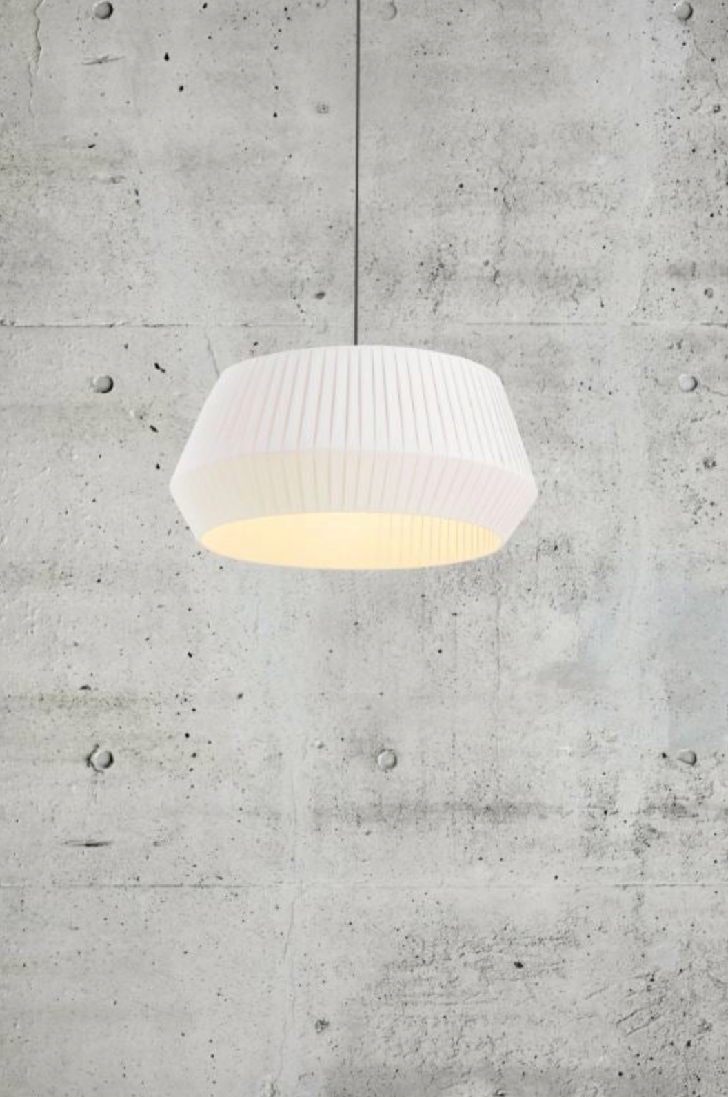 White pendant light hanging against a concrete wall