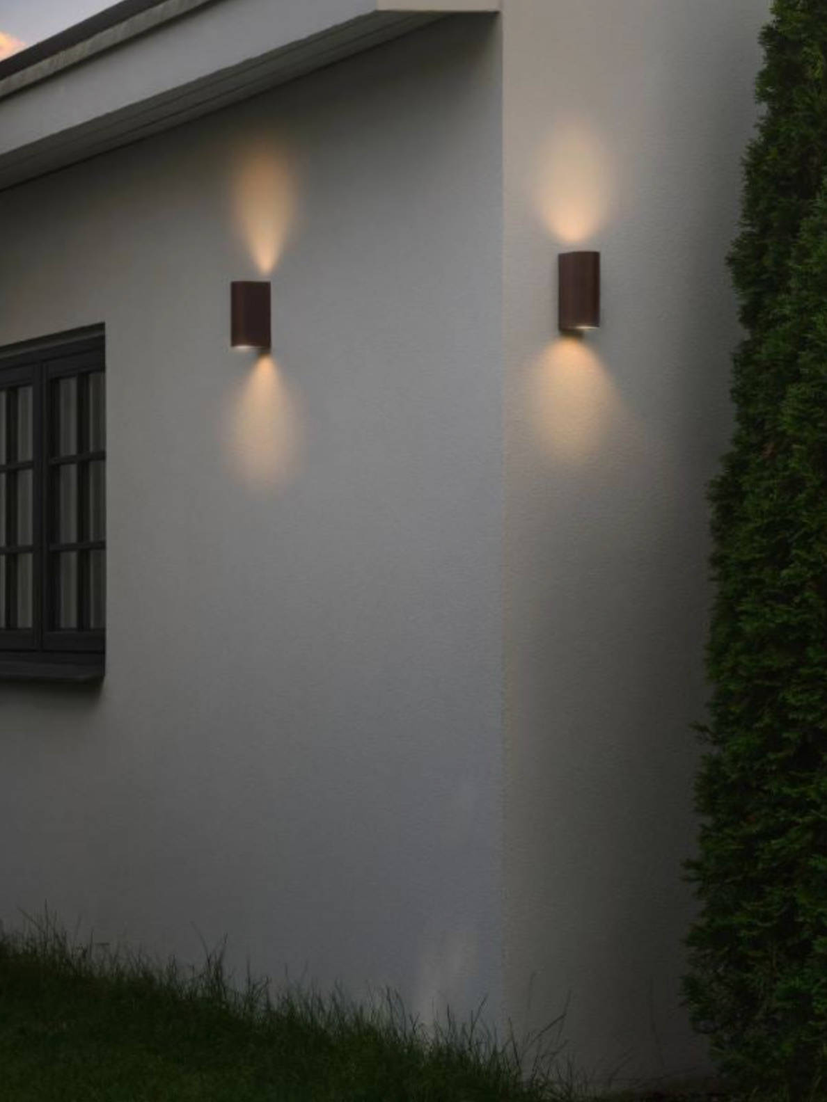 Two outdoor wall lights on a house exterior with grass and shrubbery.