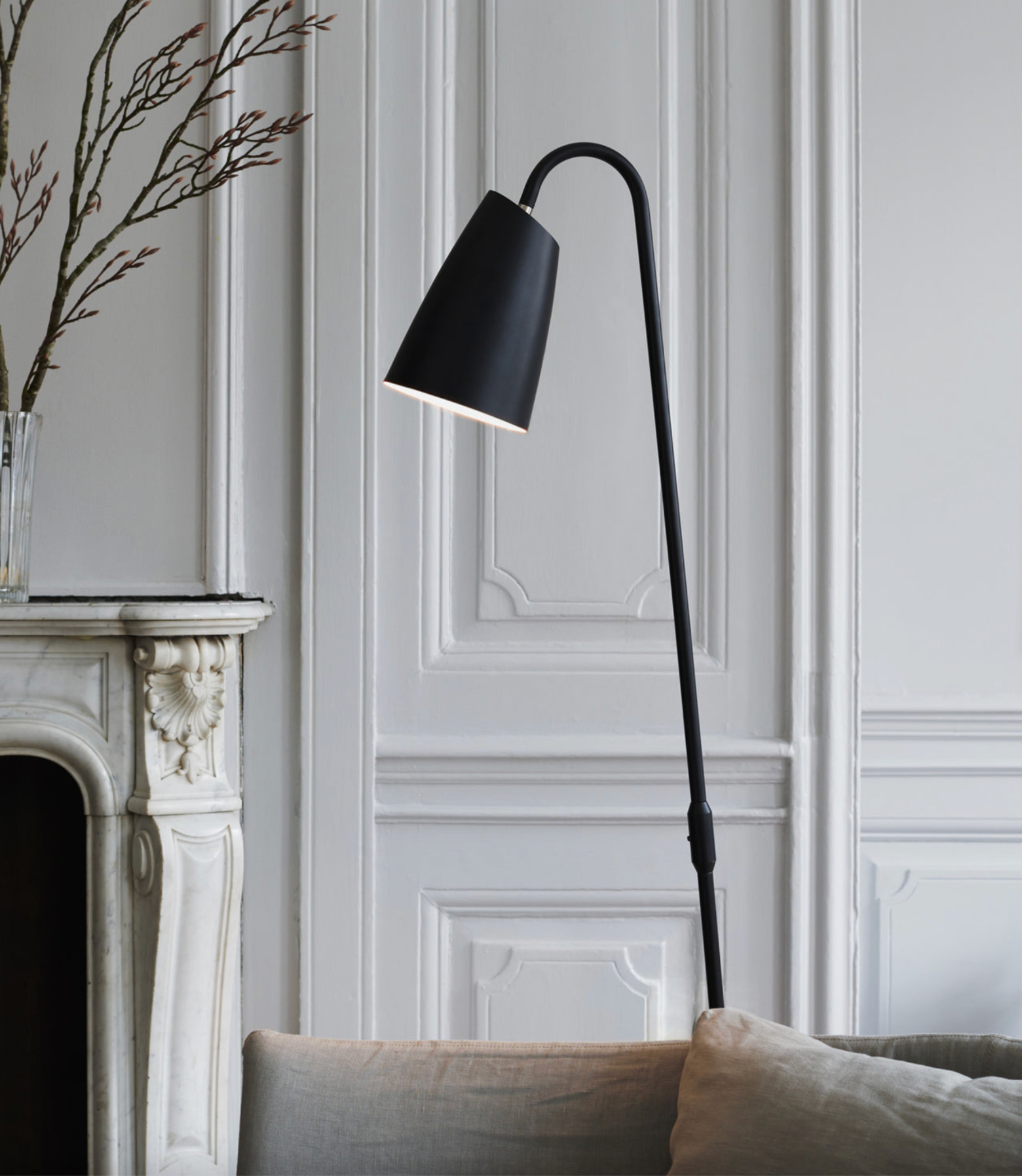 Black floor lamp in a room with white paneled walls and a fireplace.