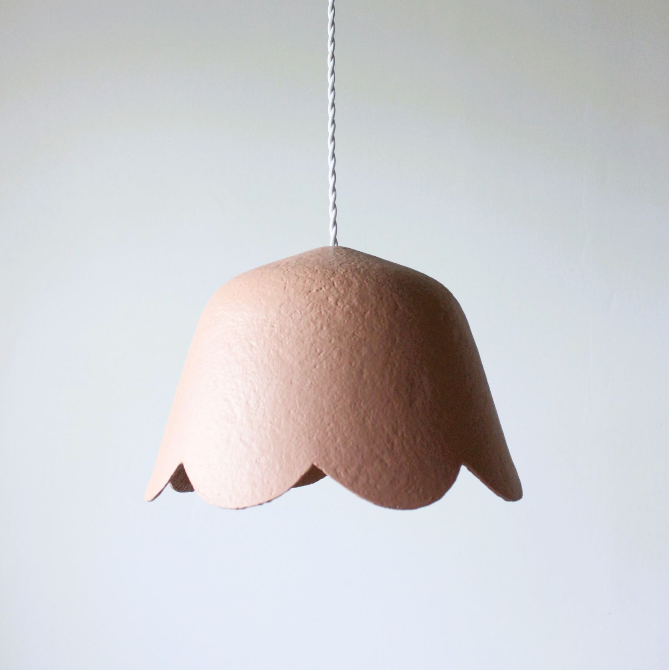 Pink handmade papier-mâché pendant light on a white background