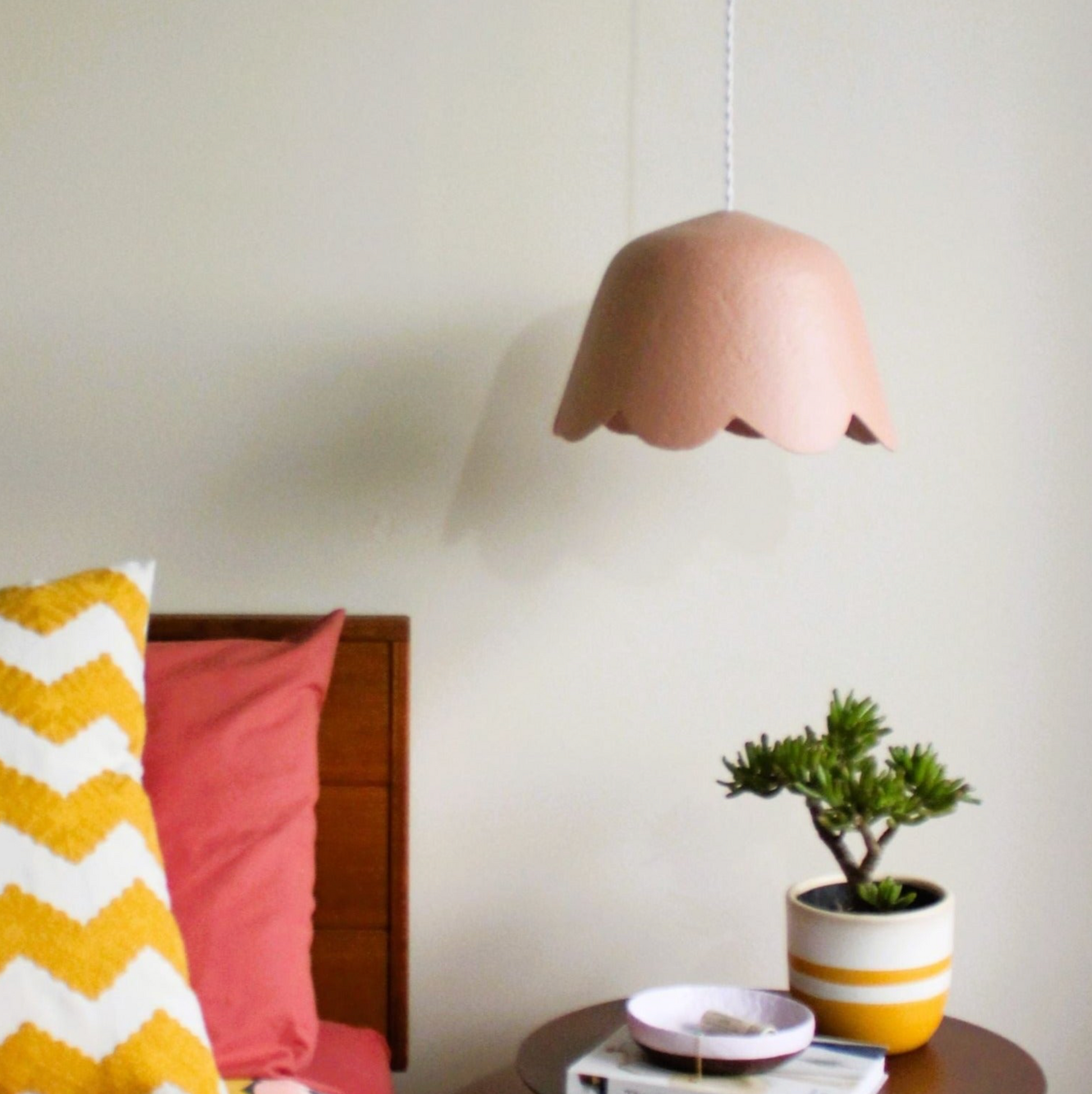 Pink handmade pendant lamp hanging above a table with a plant and books in a room.