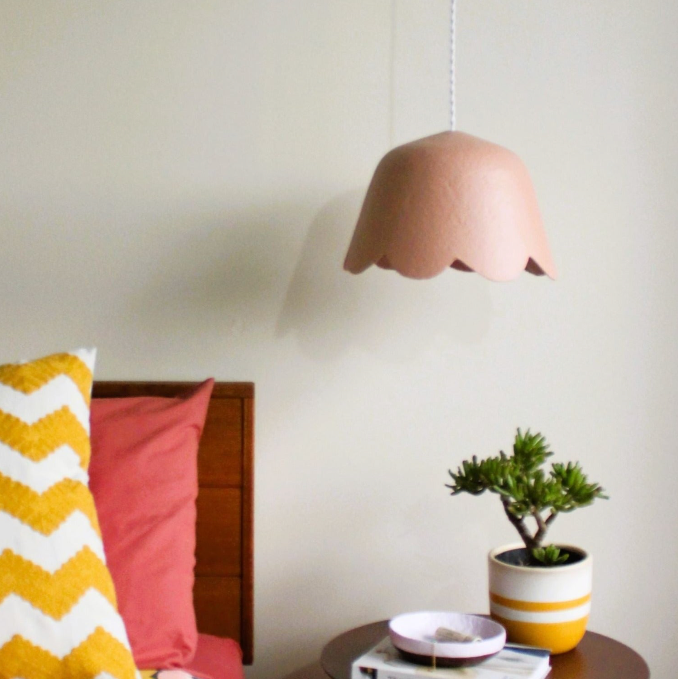 Pink handmade pendant lamp hanging above a table with a plant and books in a room.