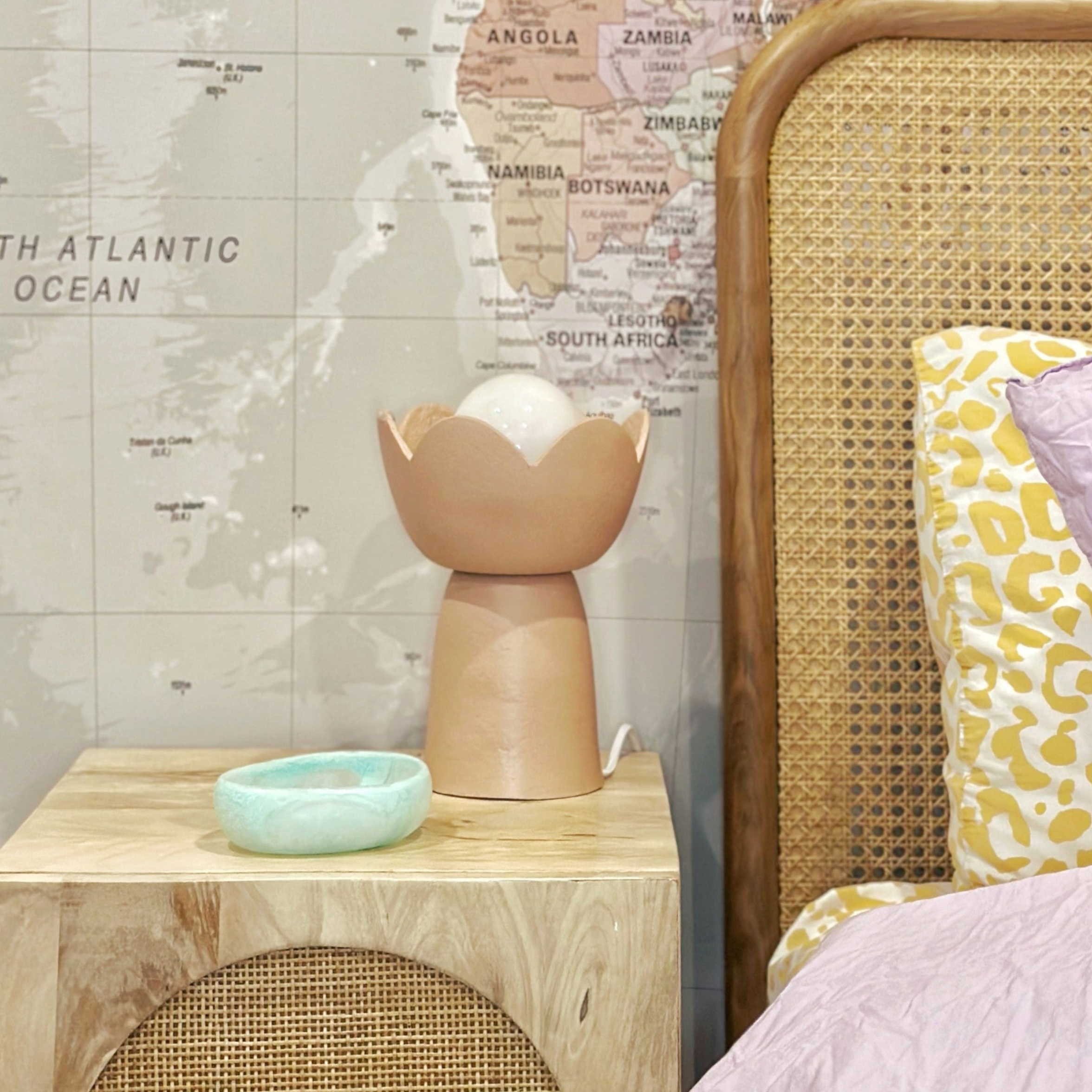 Decorative lamp on a wooden table with a wicker chair and map wall in the background