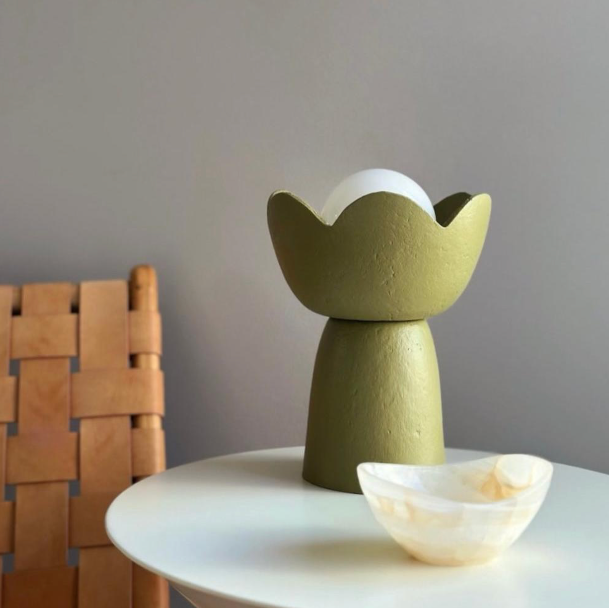 Green ceramic vase on a white surface with a wooden chair in the background
