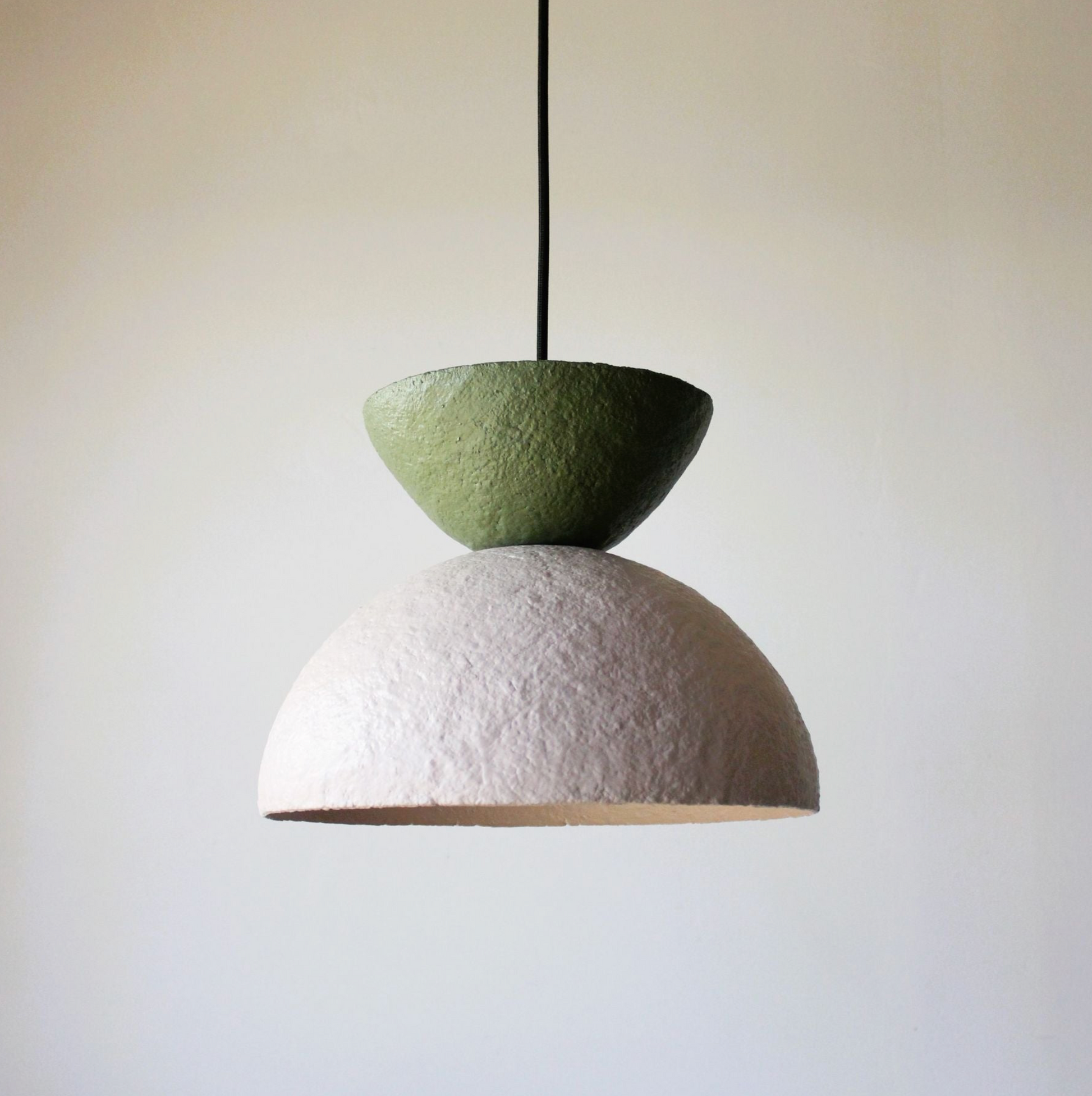 Two-tiered handmade pendant light with green top and white bottom on a plain background