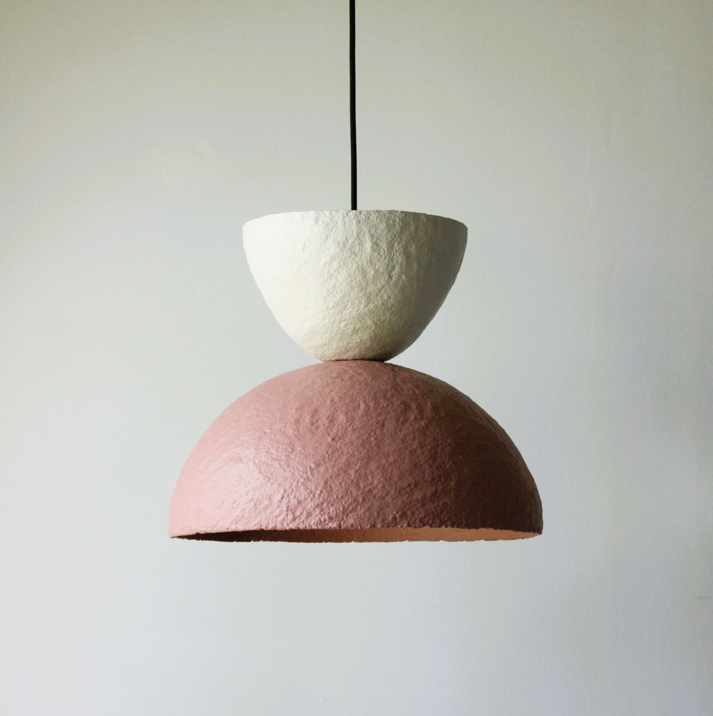 Two-toned pendant lamp with white upper half and pink lower half on a plain background