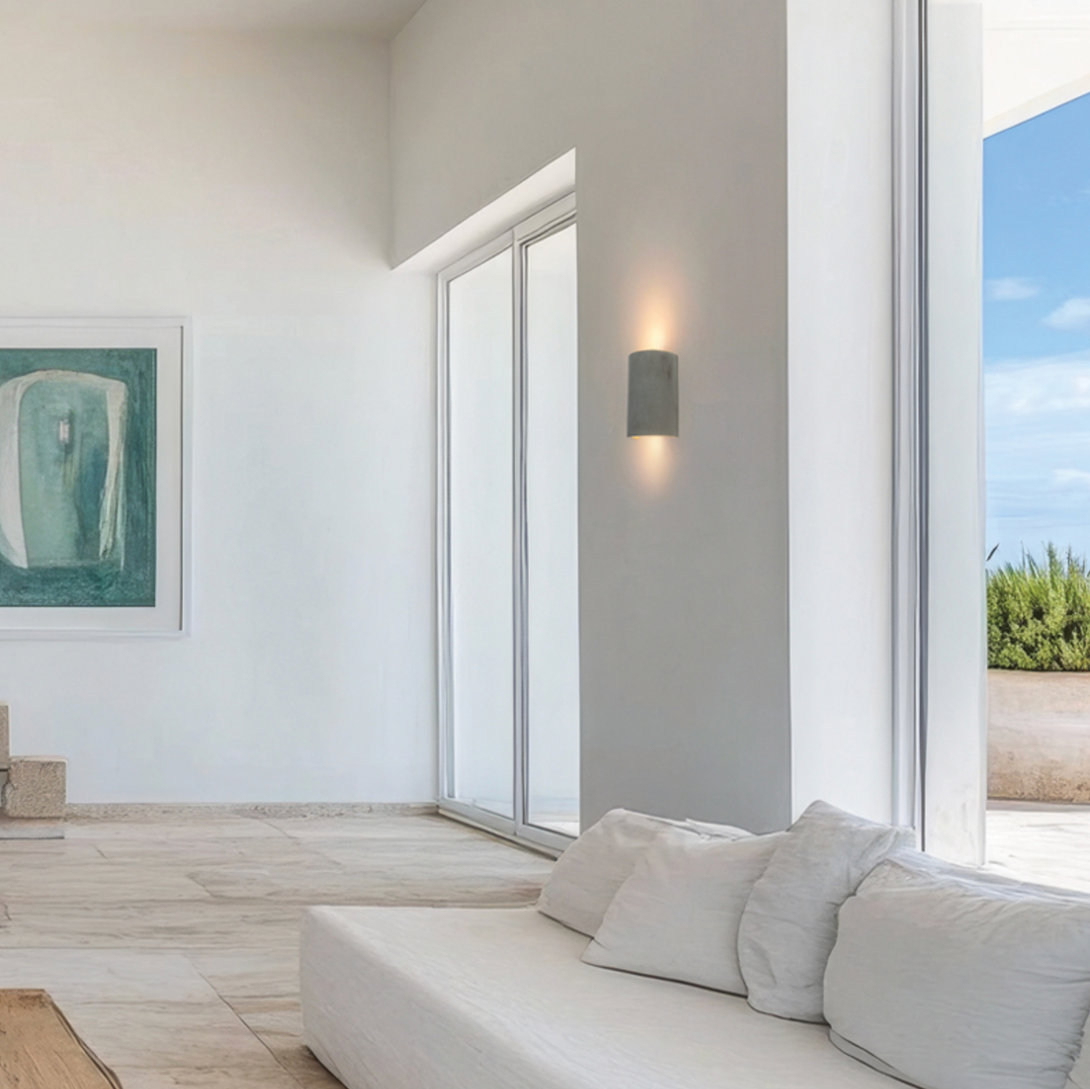 Modern living room with a white sofa, large windows, and abstract art on the wall.