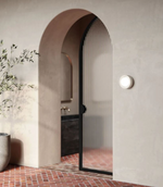 Archway leading to a bathroom with a black door and light fixture on the wall.