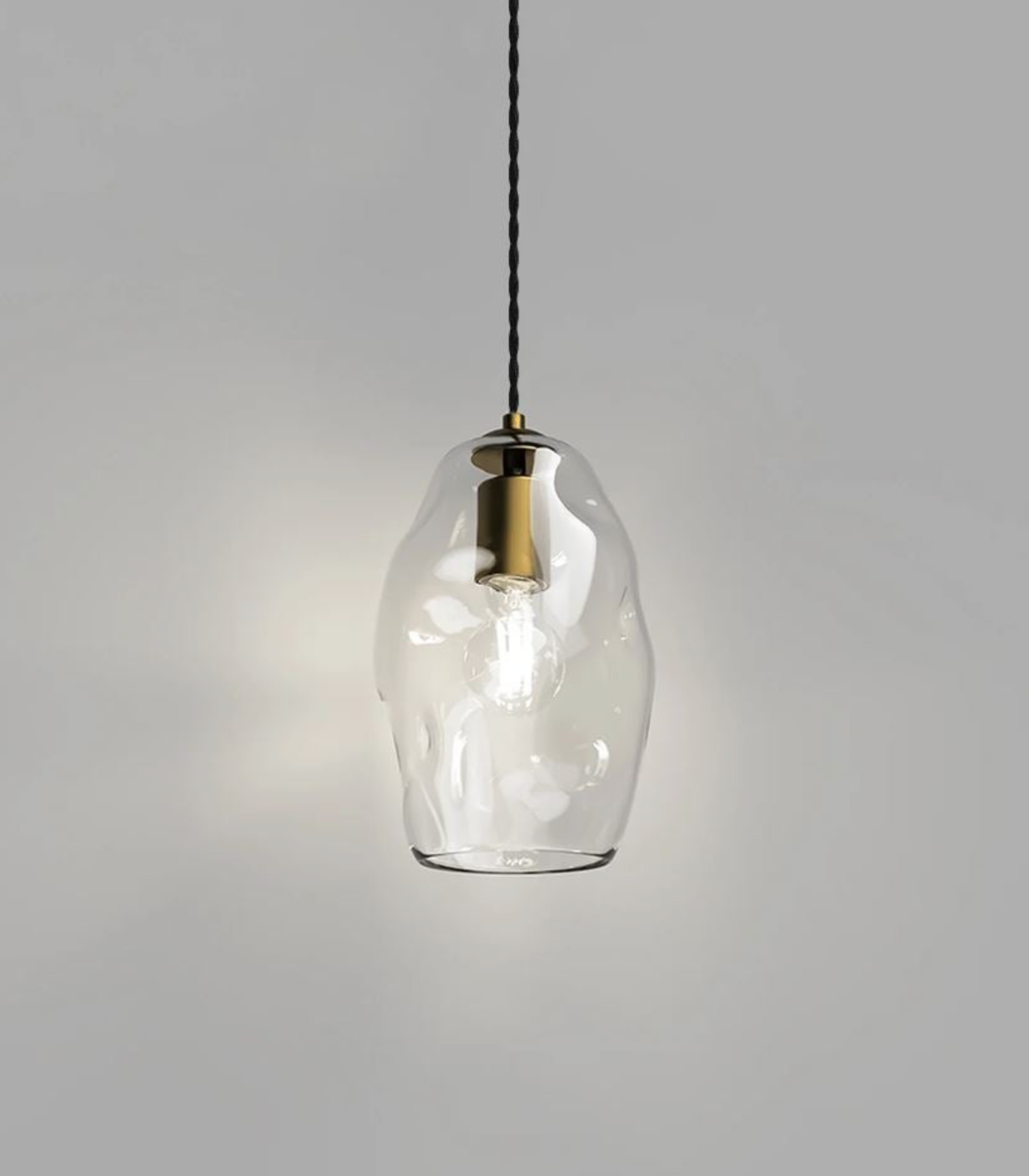 Clear glass pendant light with brass fixture on a gray background