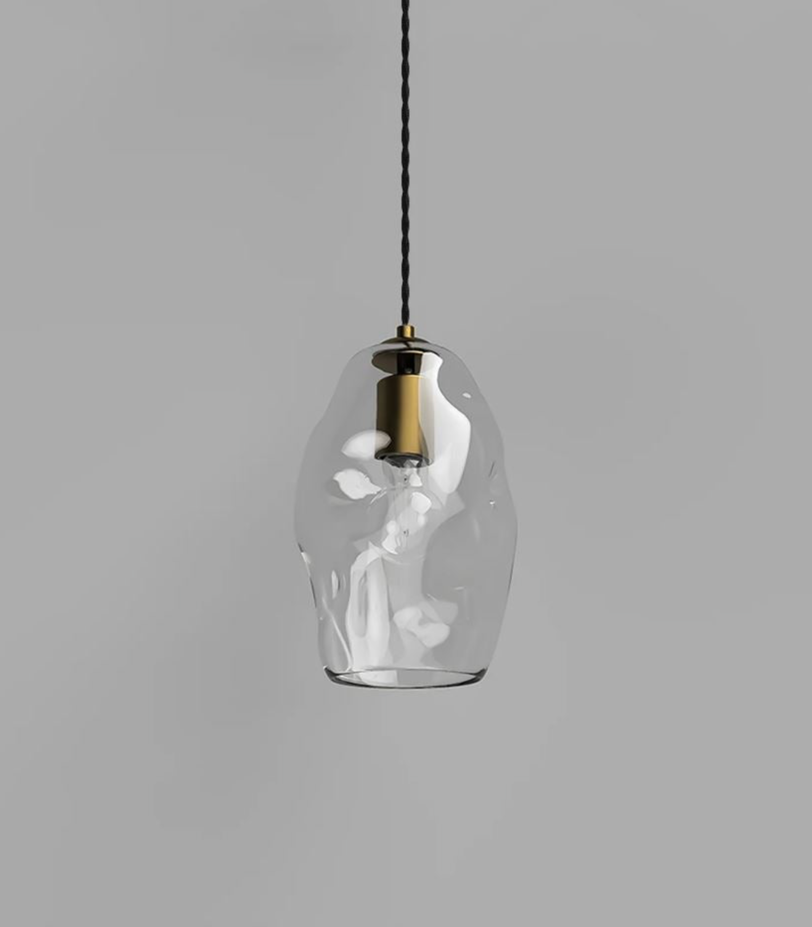 Clear glass pendant light with brass fixture on a gray background