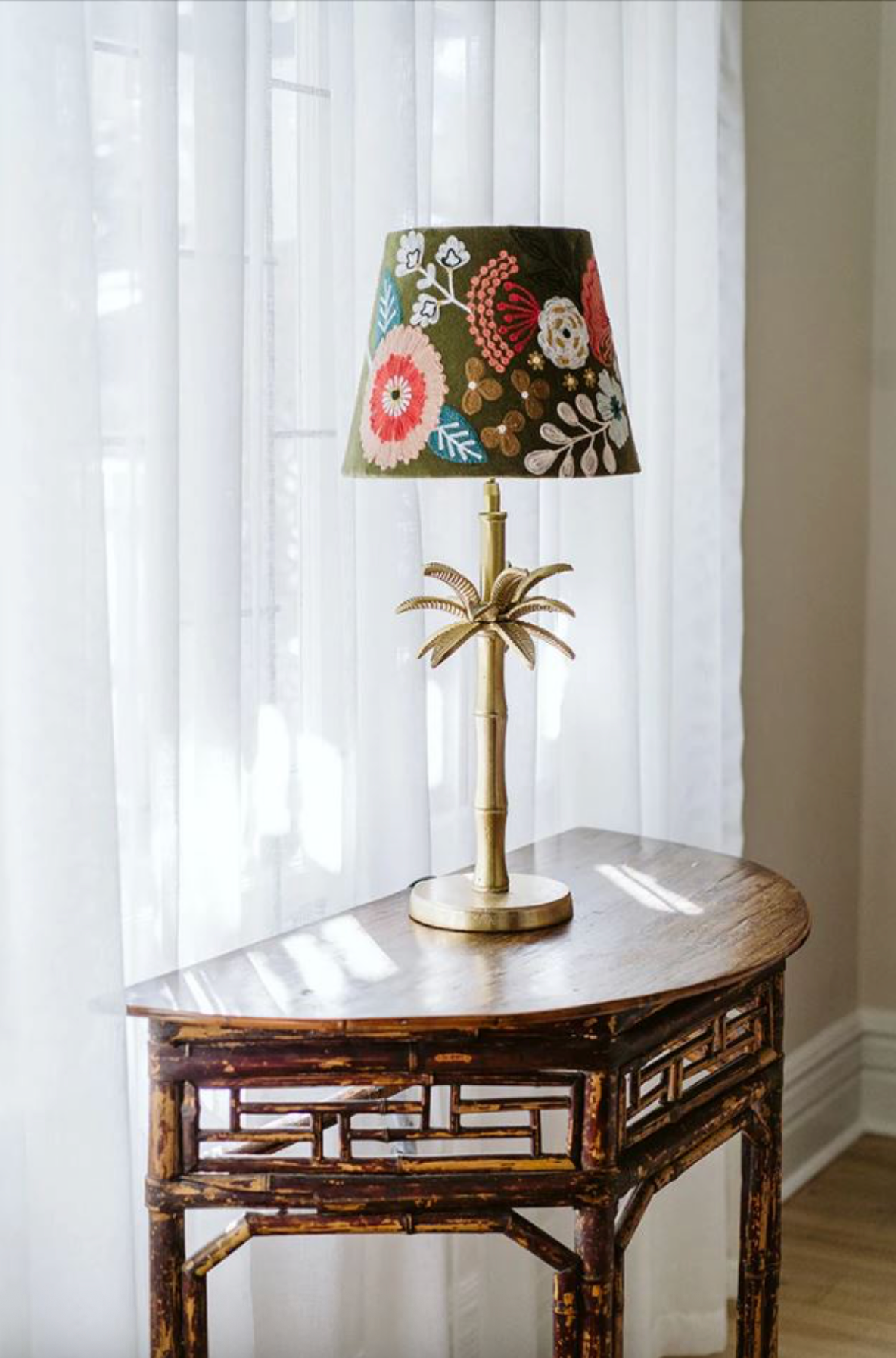 Decorative lamp with floral shade on a wooden table in front of sheer curtains