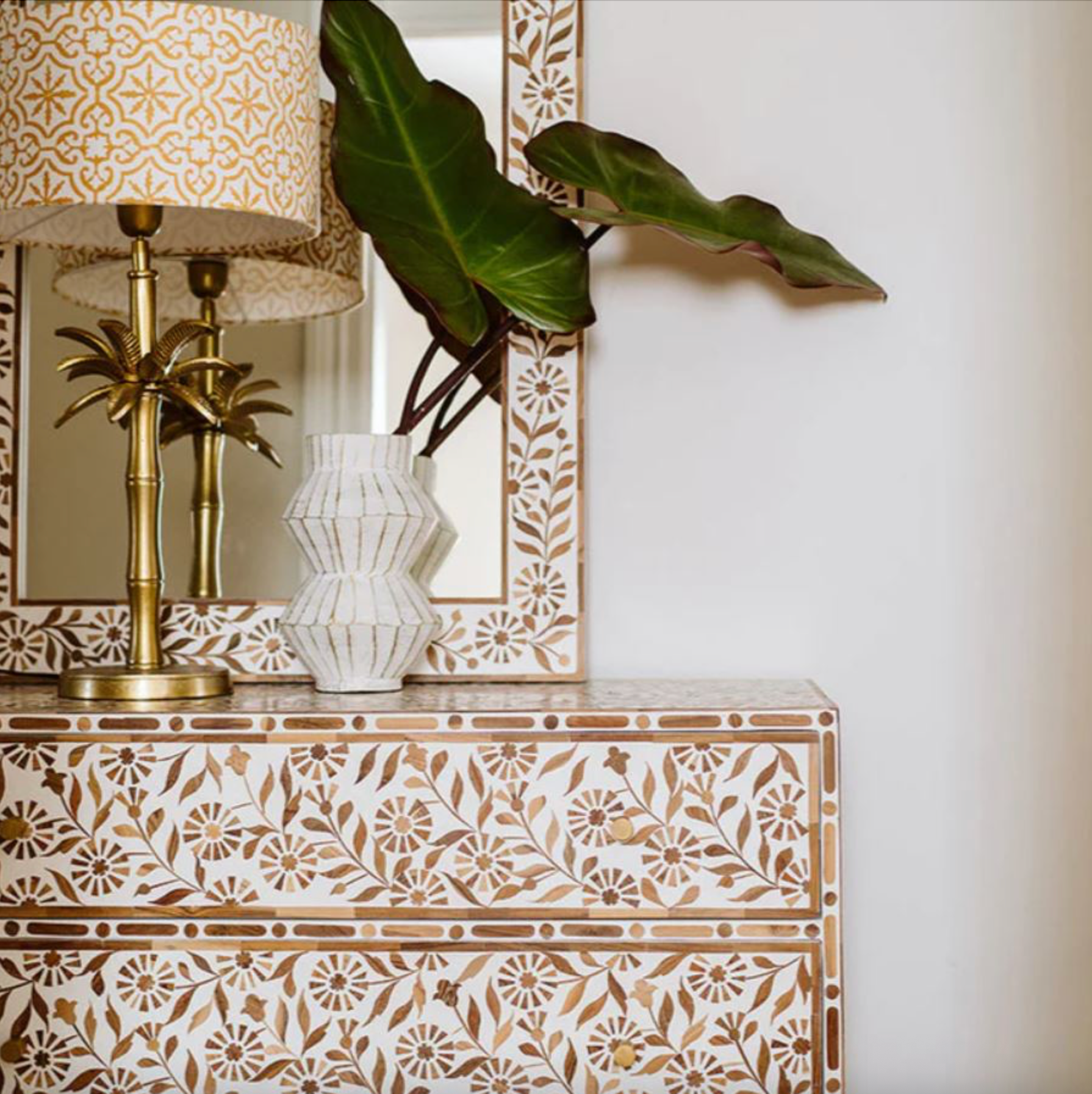 Decorative cabinet with floral patterns, lamp, and plant in a room setting.