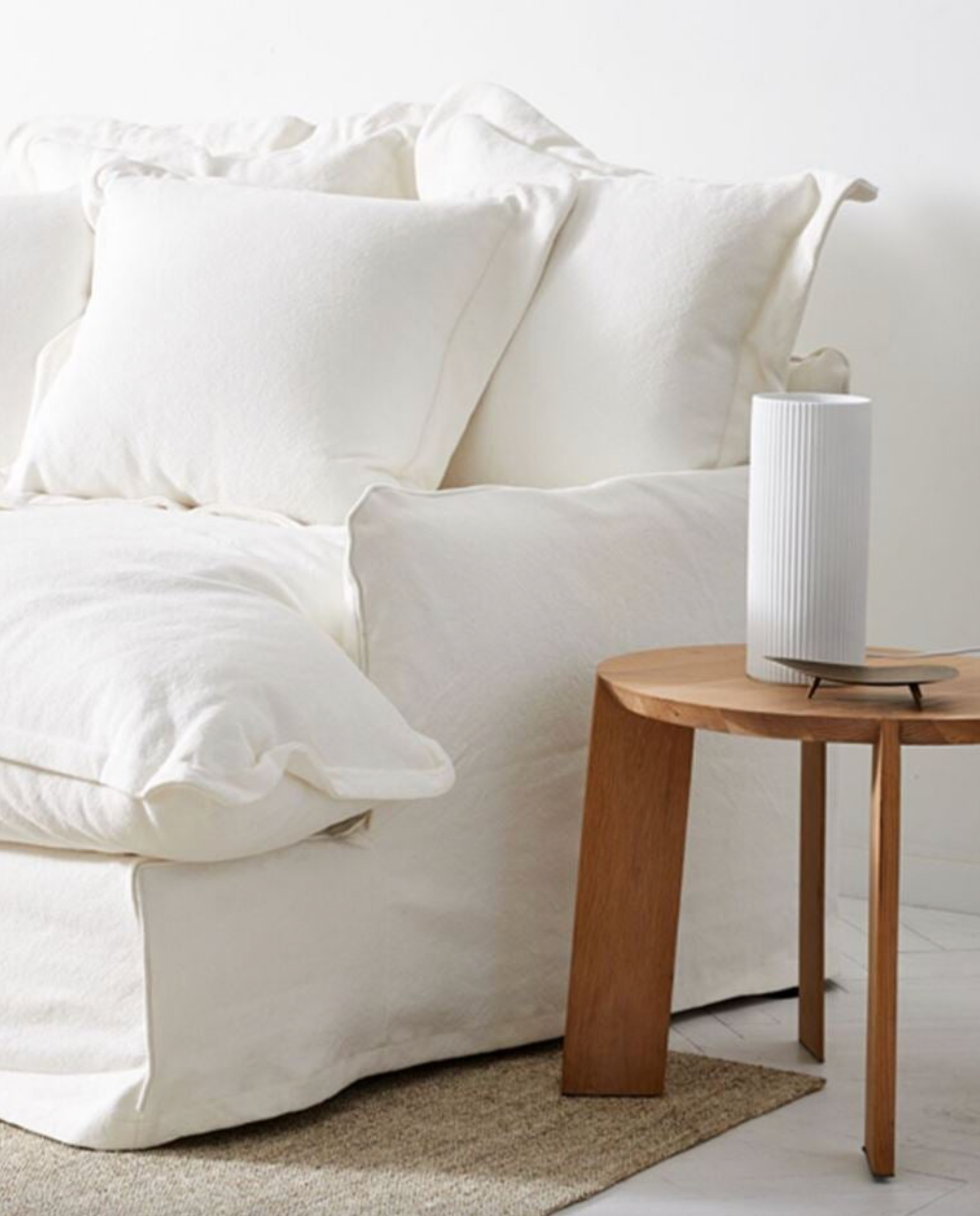 White sofa with cushions and a wooden side table in a minimalistic living room.