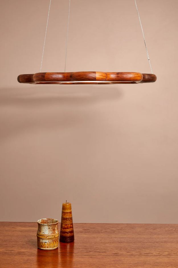 Wavy wooden pendant light fixture on a beige wall with a wooden surface below.