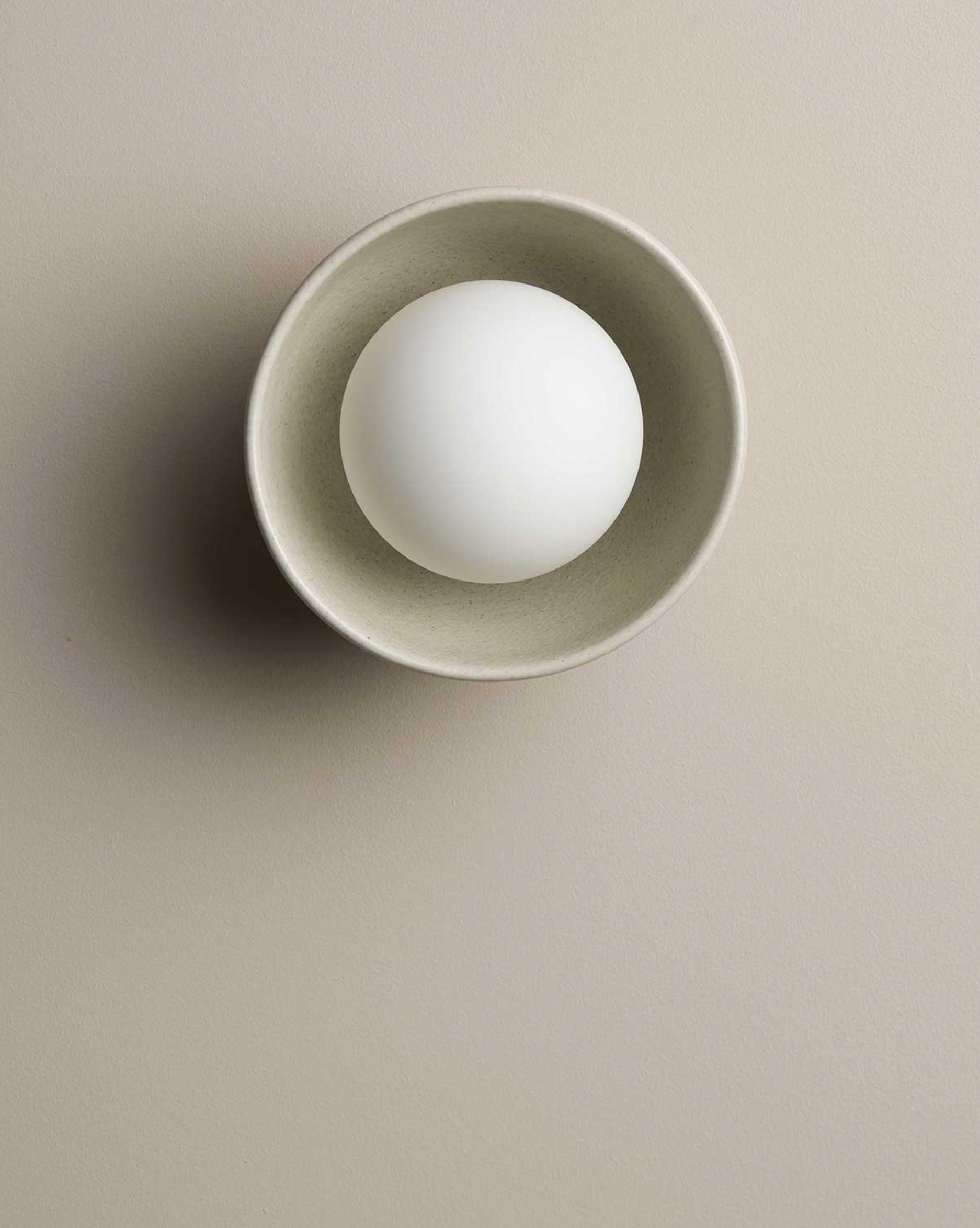 White orb inside a beige ceramic bowl on a beige background