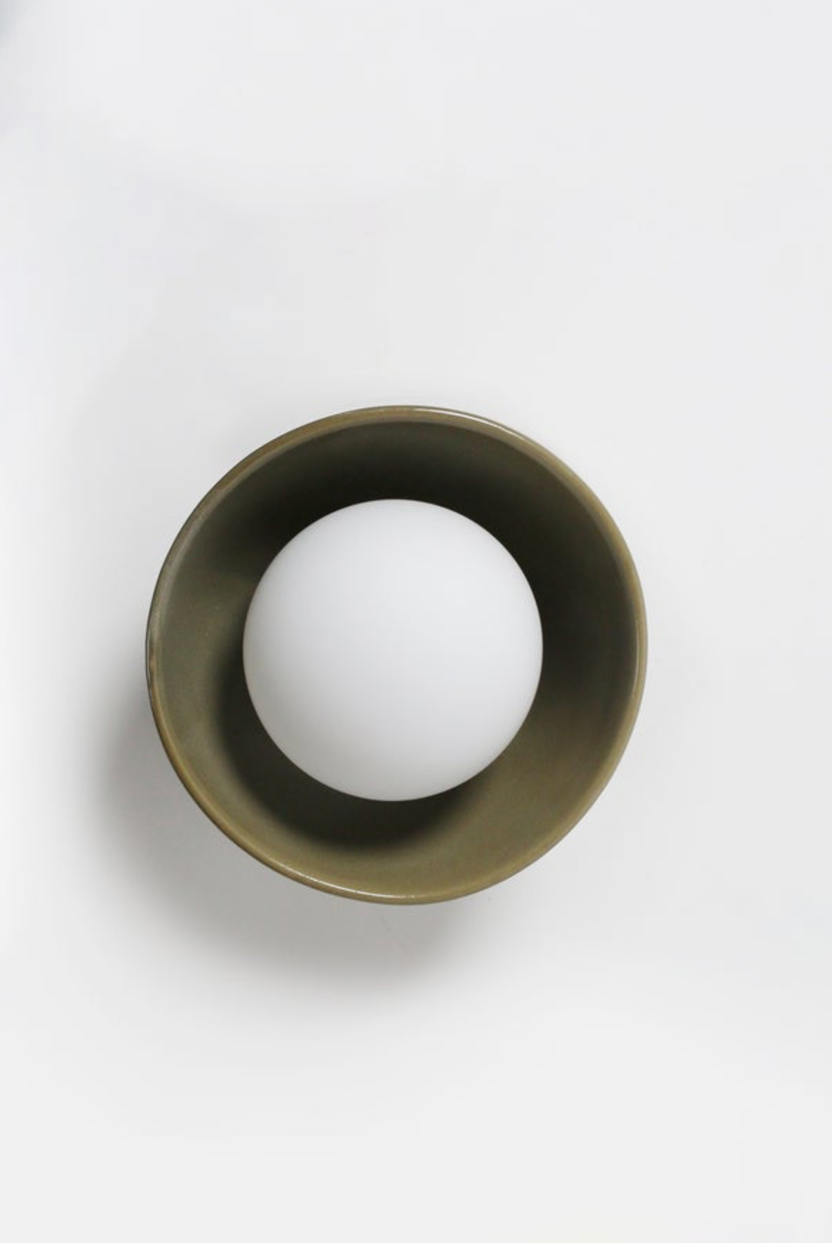 White ball inside an olive cylindrical ceramic on a white background