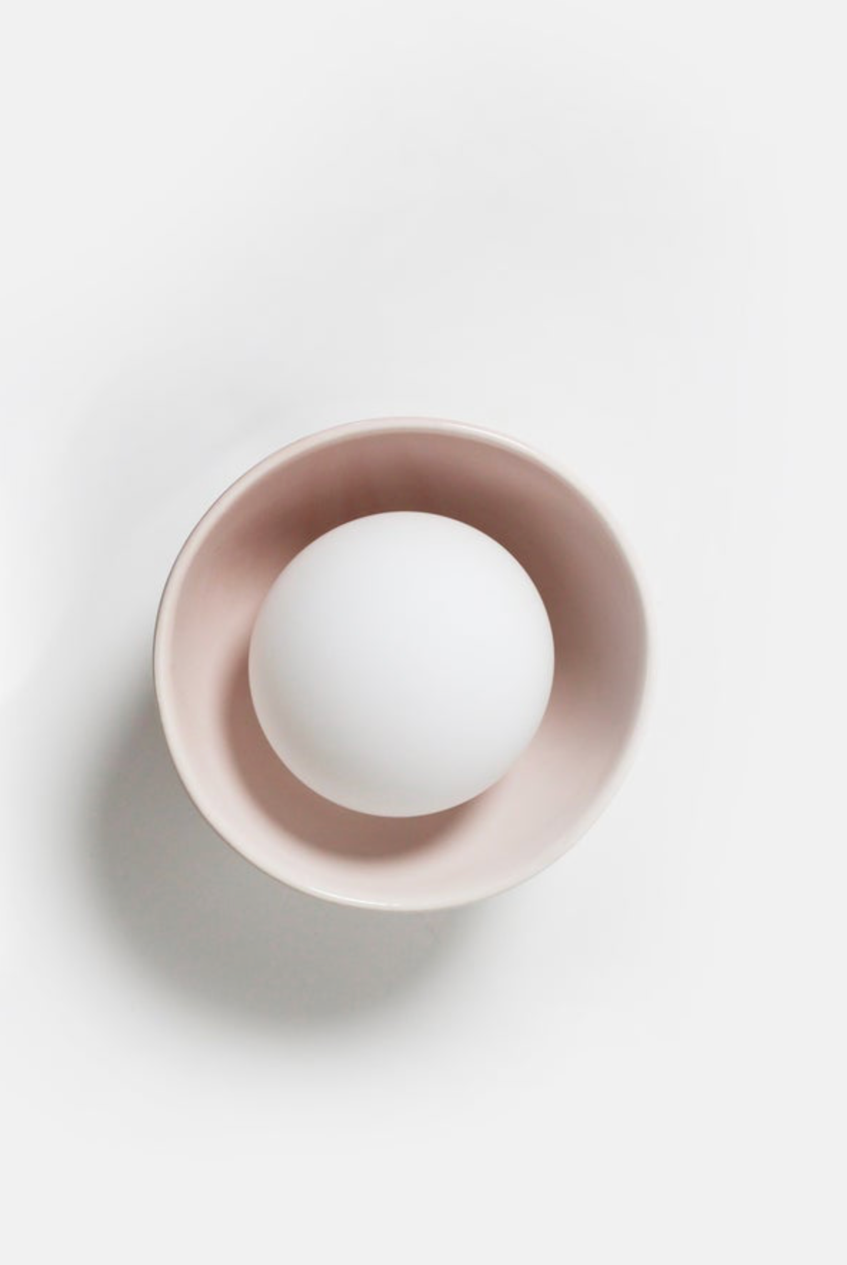 White orb interior wall light inside a pink bowl on a light white background