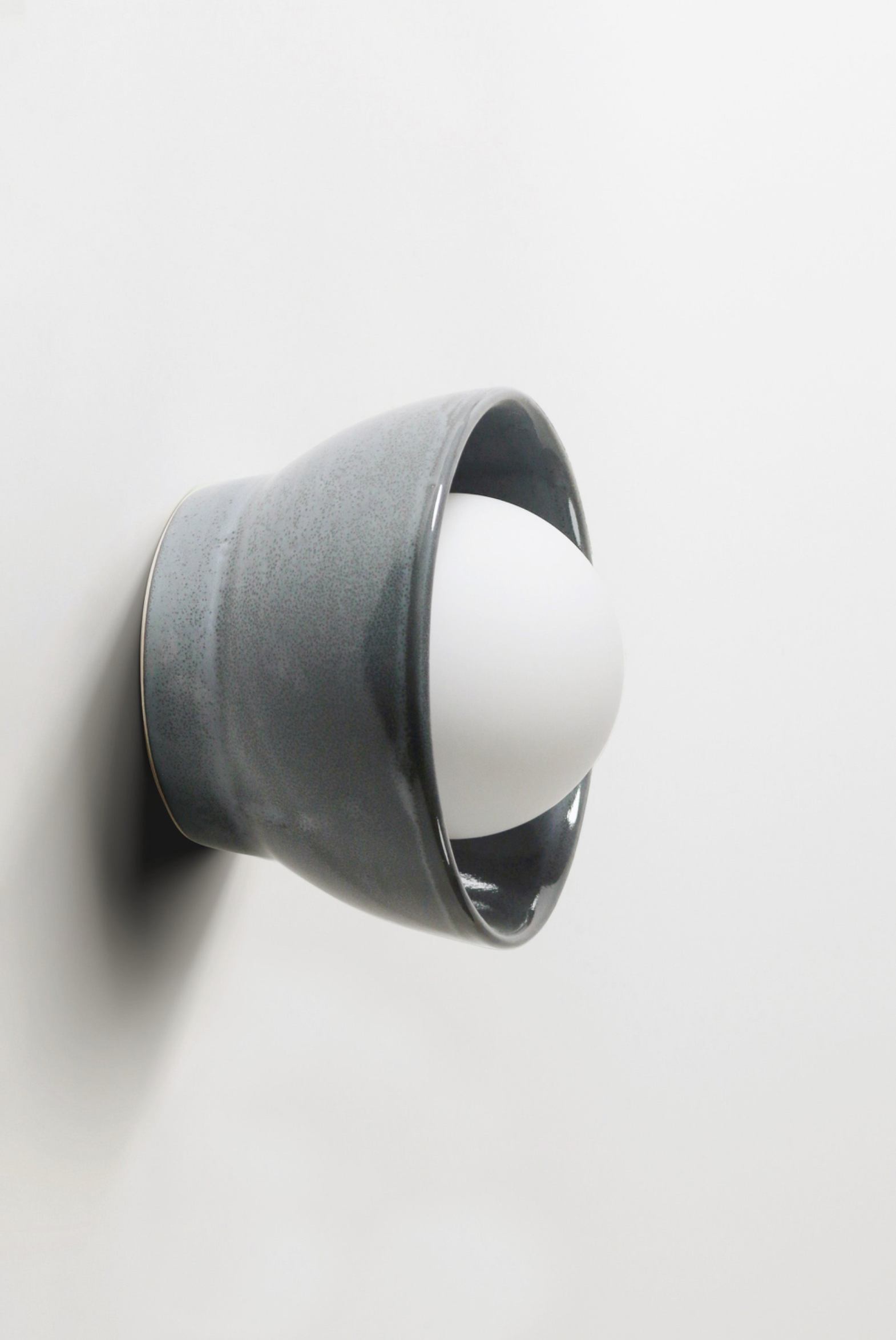 Wall-mounted ceramic light fixture with a white bulb on a plain background