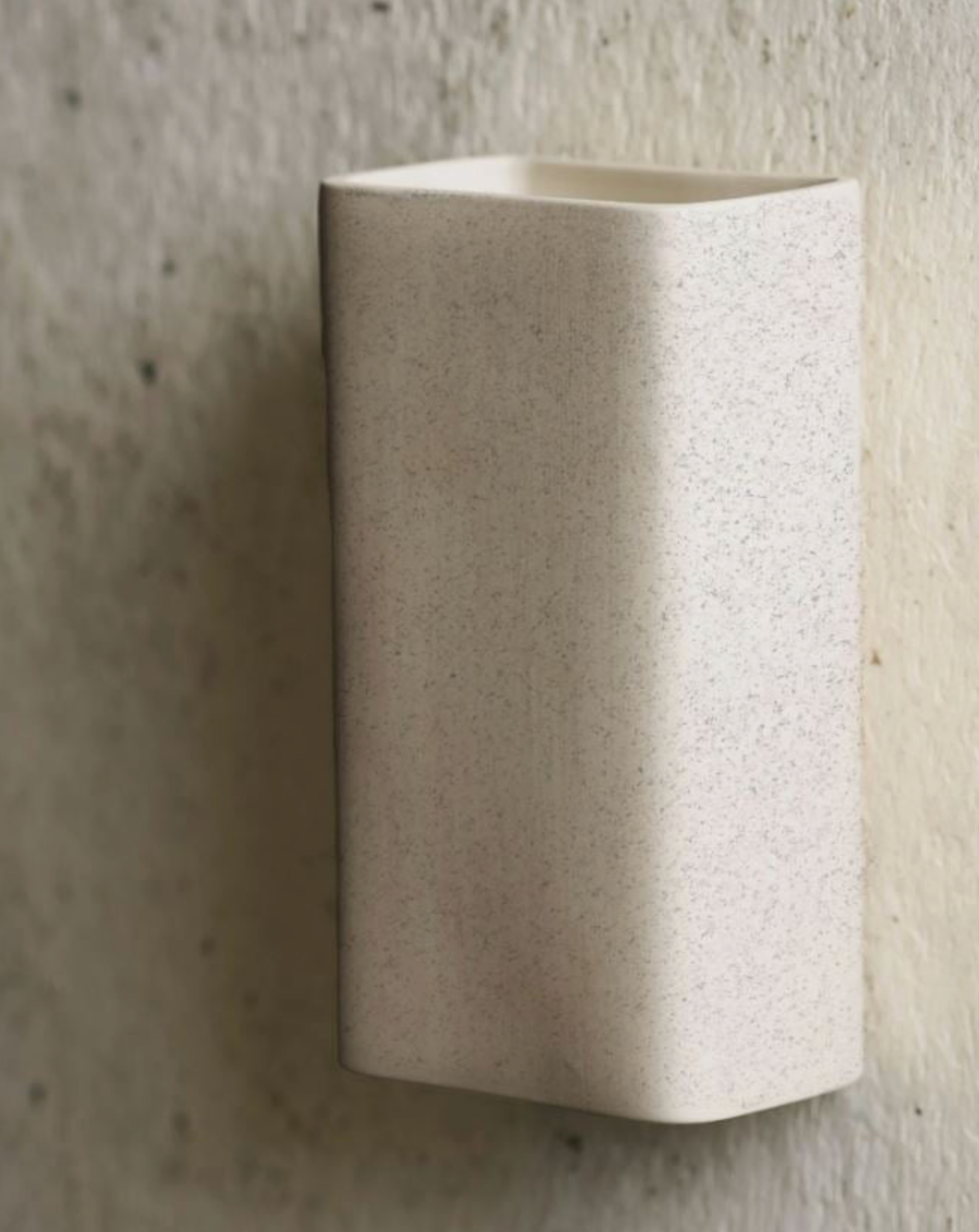Beige ceramic sconce against a textured wall