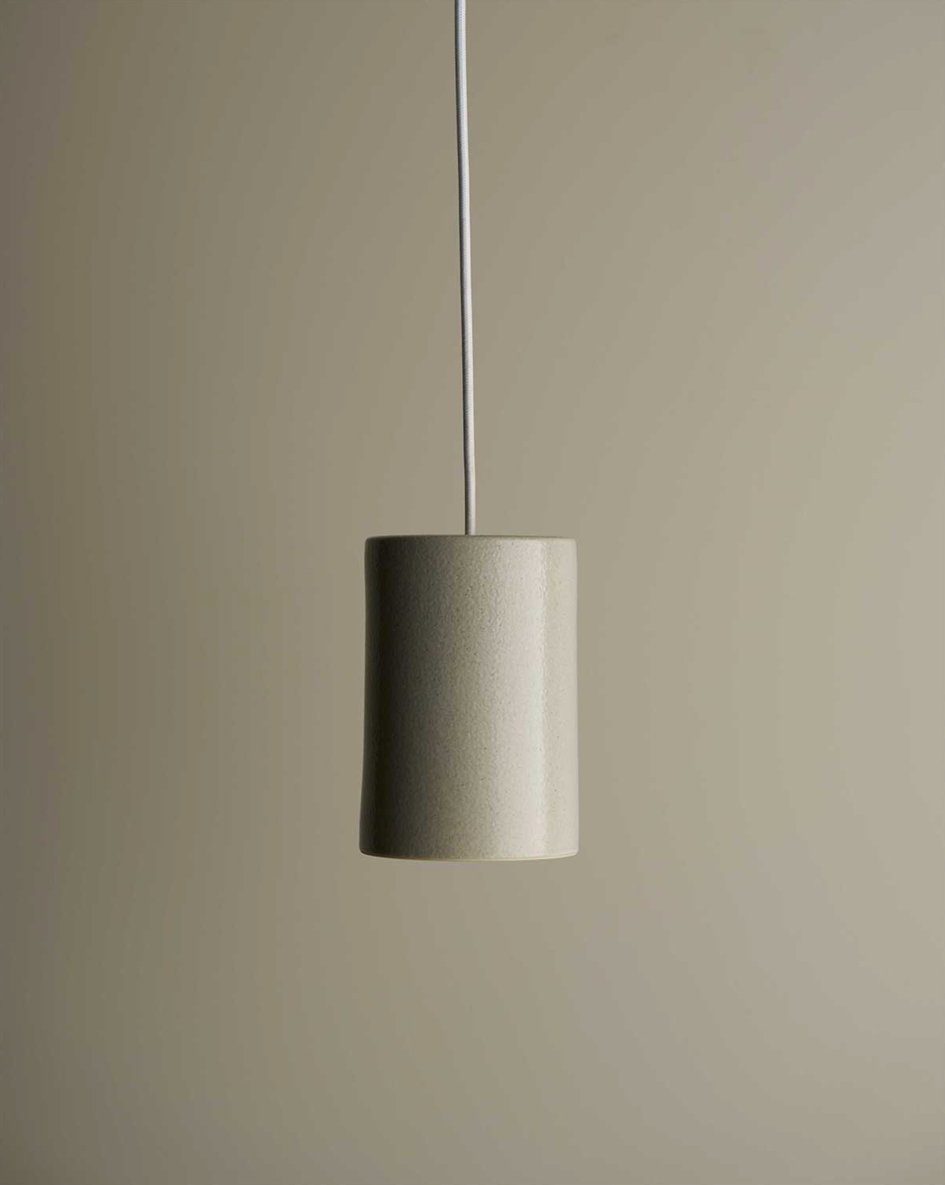 Minimalist ceramic pendant light with a cylindrical shade on a plain background