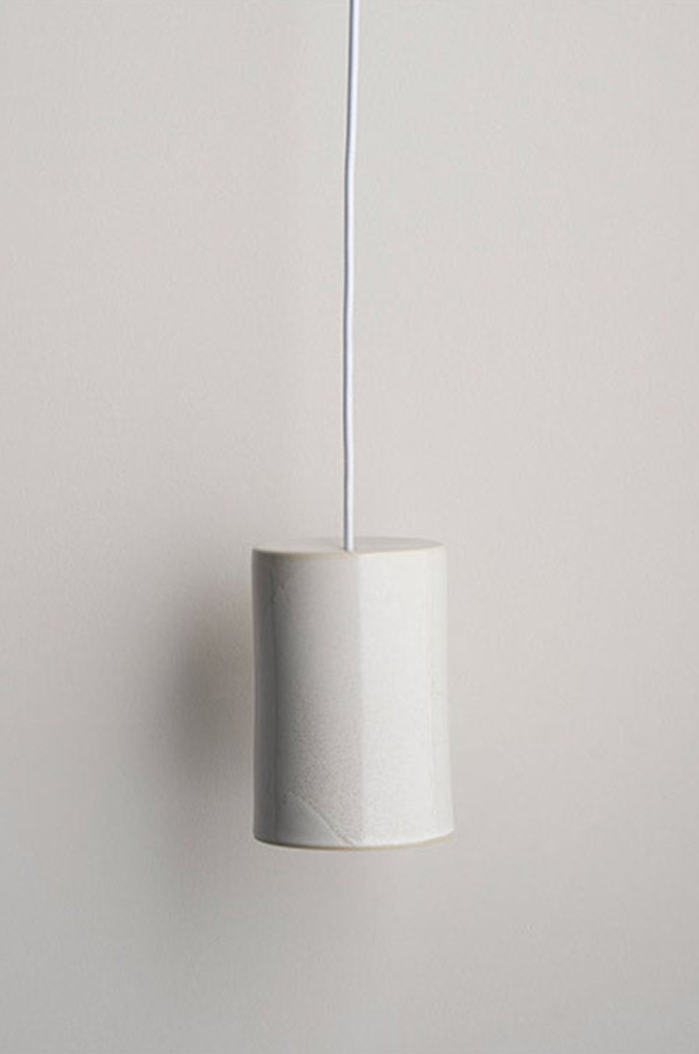 Minimalist ceramic pendant light with a cylindrical shade on a plain background