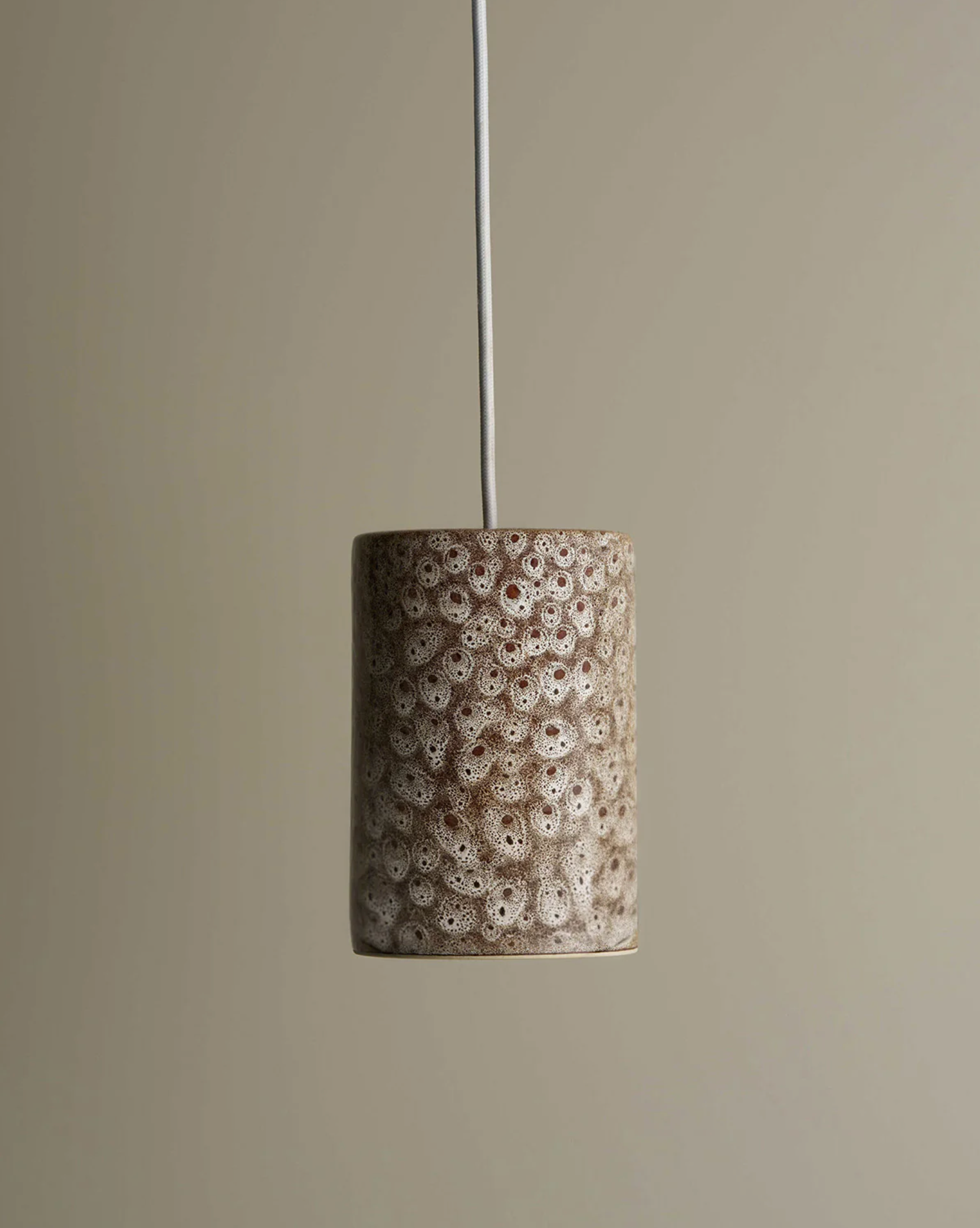 Cylindrical ceramic pendant light with textured brown pattern on a beige background