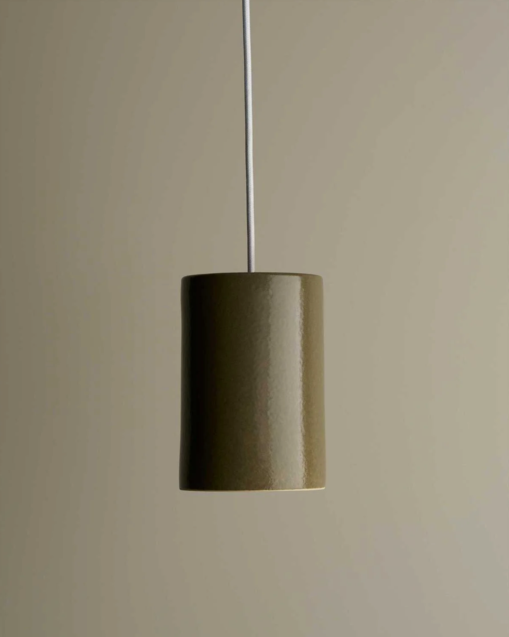 Cylindrical ceramic pendant light hanging against a plain wall