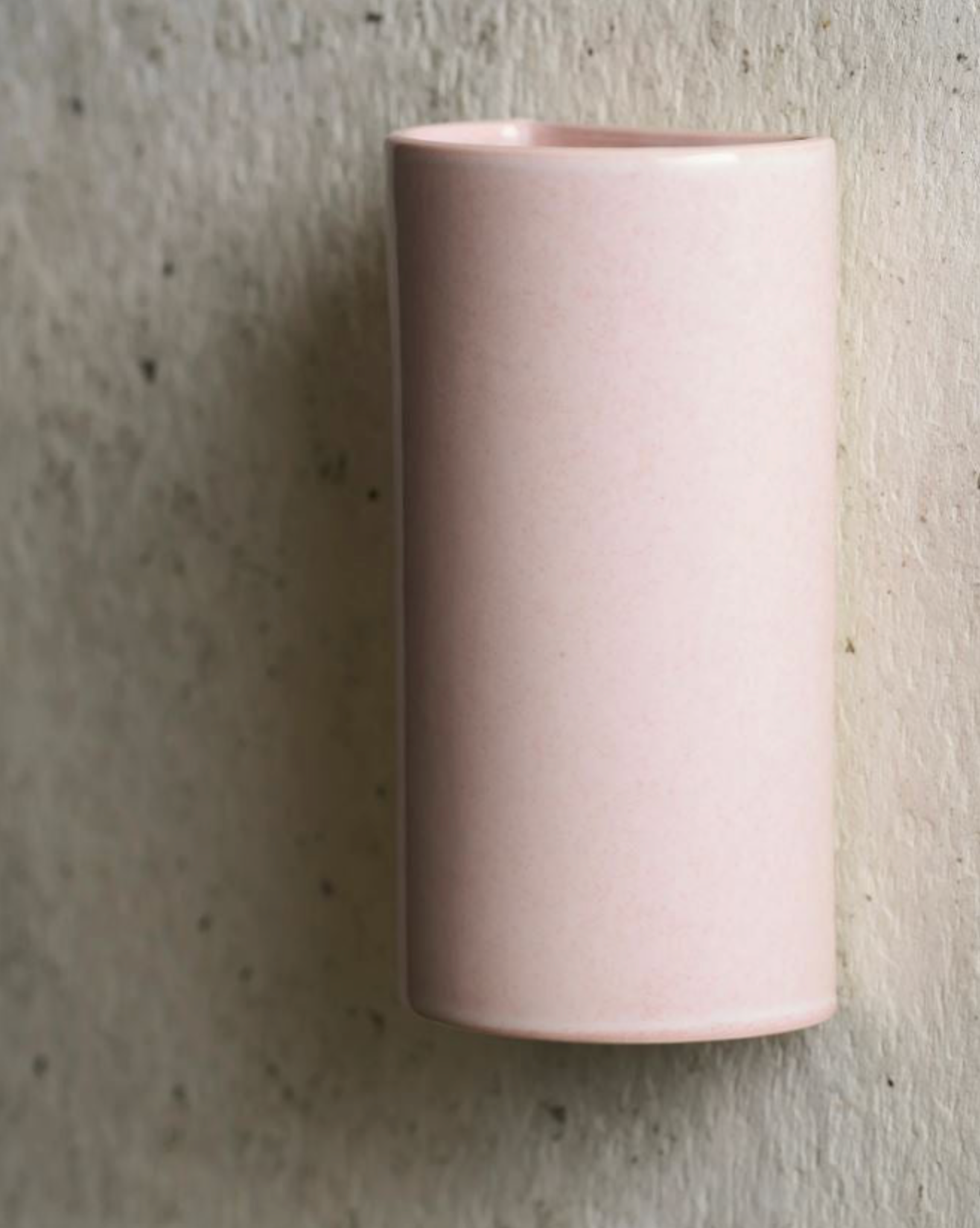 Pink cylindrical ceramic wall light against a textured grey wall
