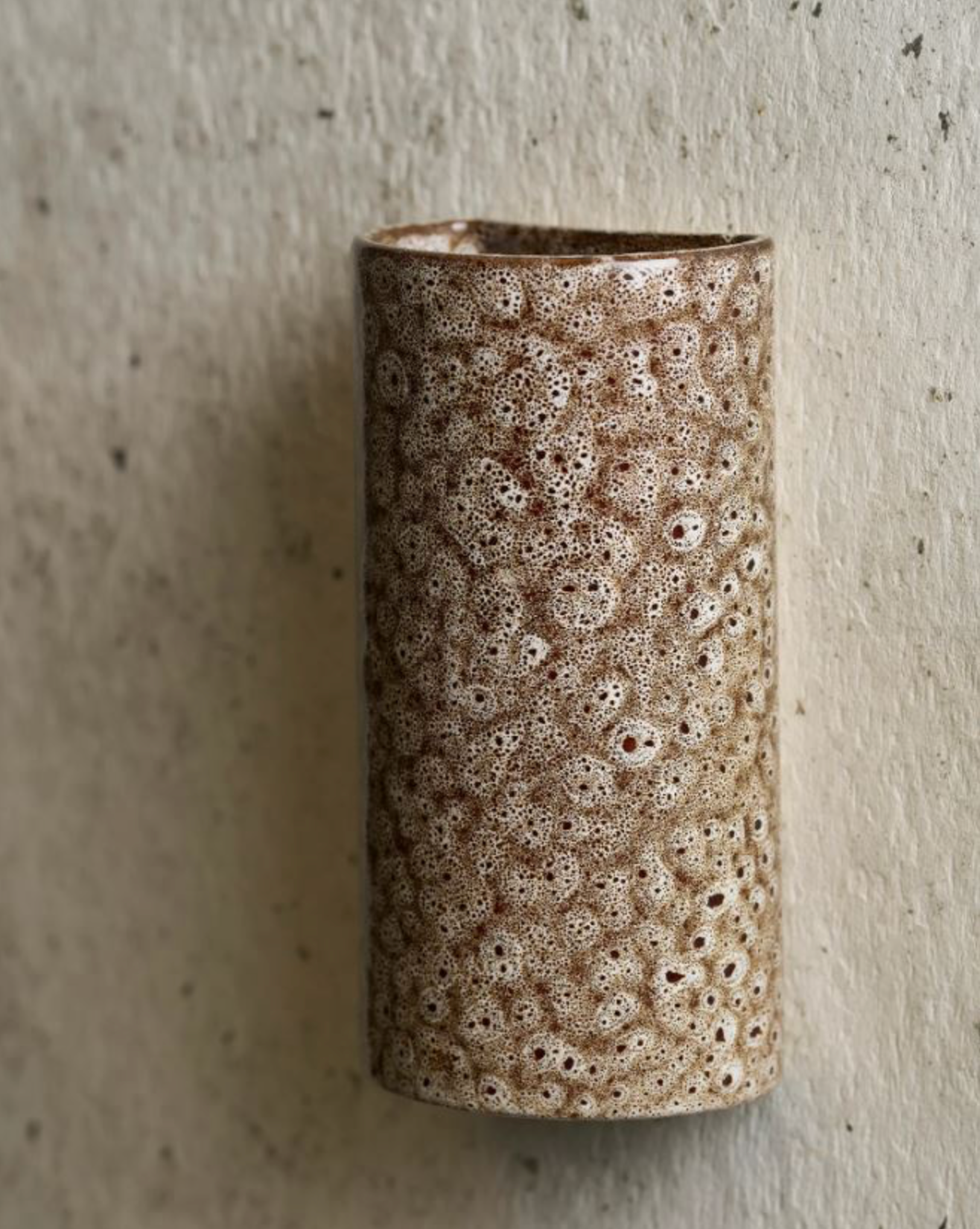 Cylindrical ceramic wall sconce with textured surface on a gray background