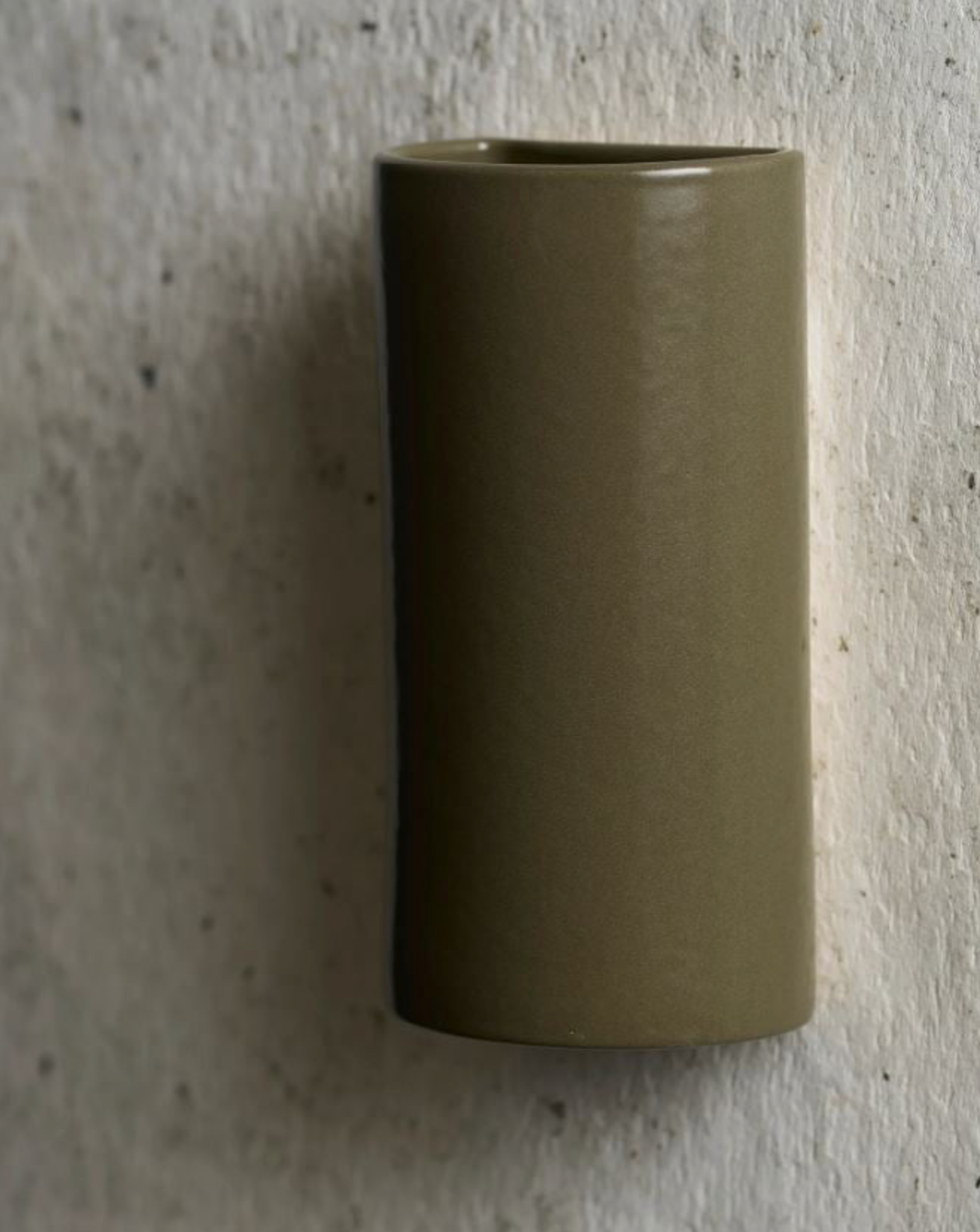 Cylindrical ceramic sconce in a neutral olive colour on a textured wall.
