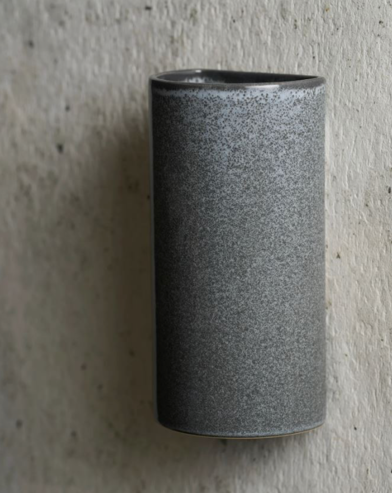 Cylindrical grey ceramic textured sconce on a concrete surface