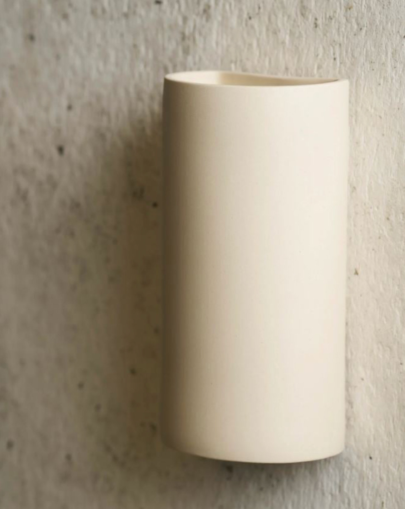 Beige cylindrical ceramic wall sconce on a textured grey wall